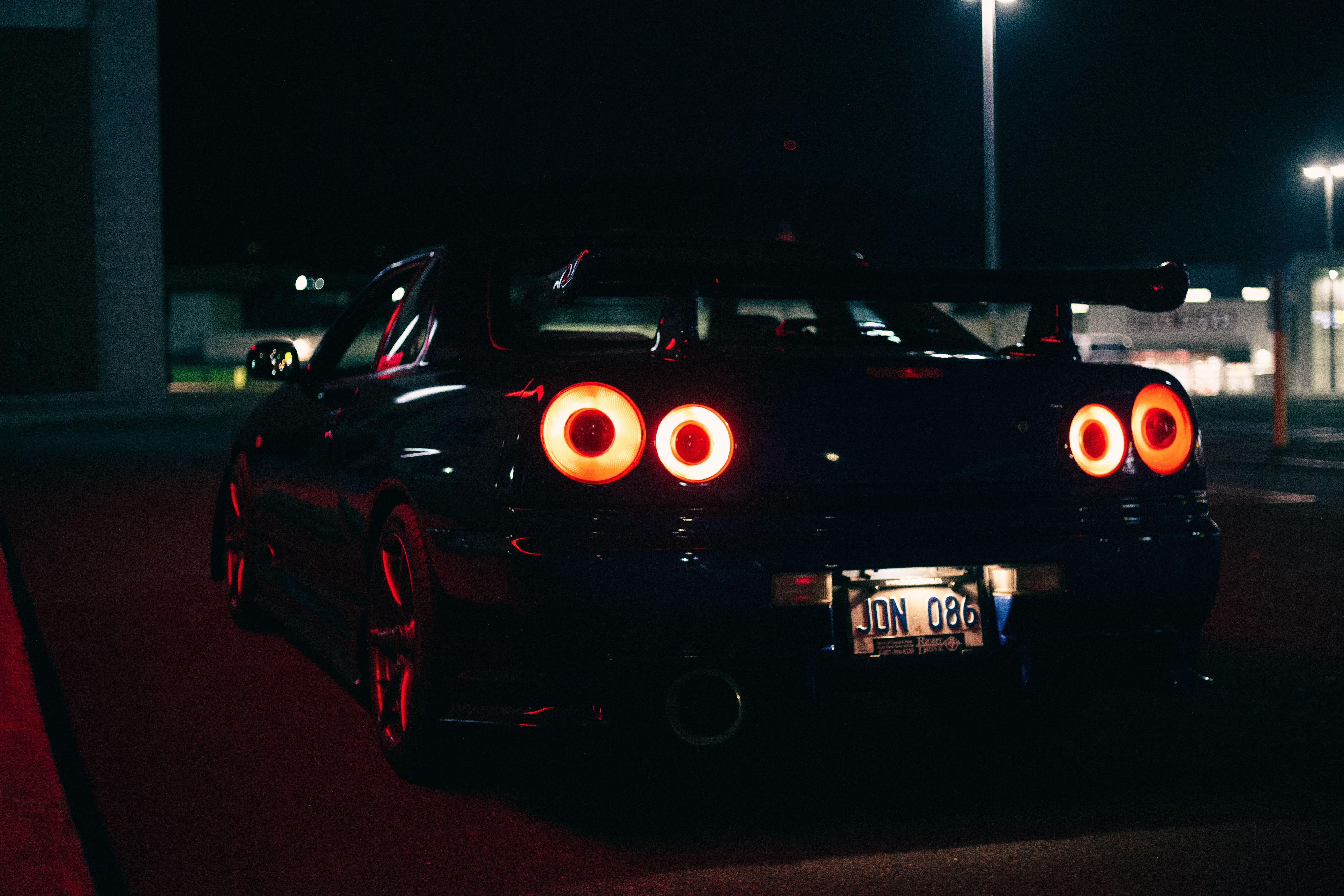 A black sports car with red lights parked in a parking lot at night. - Nissan Skyline