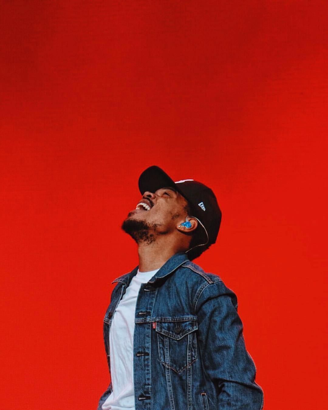 A man wearing jeans and sunglasses is holding his phone - Chance the Rapper