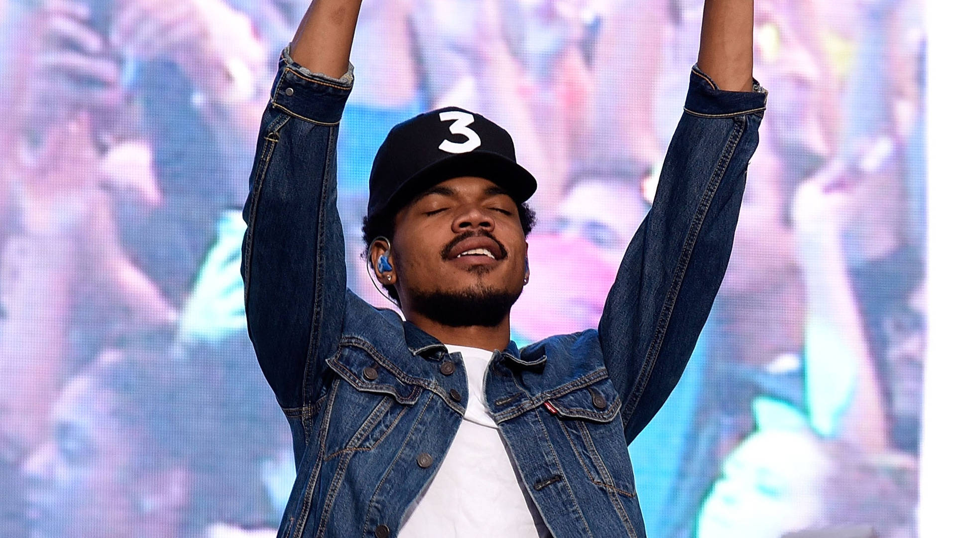 A man in denim jacket and hat raises his hands - Chance the Rapper