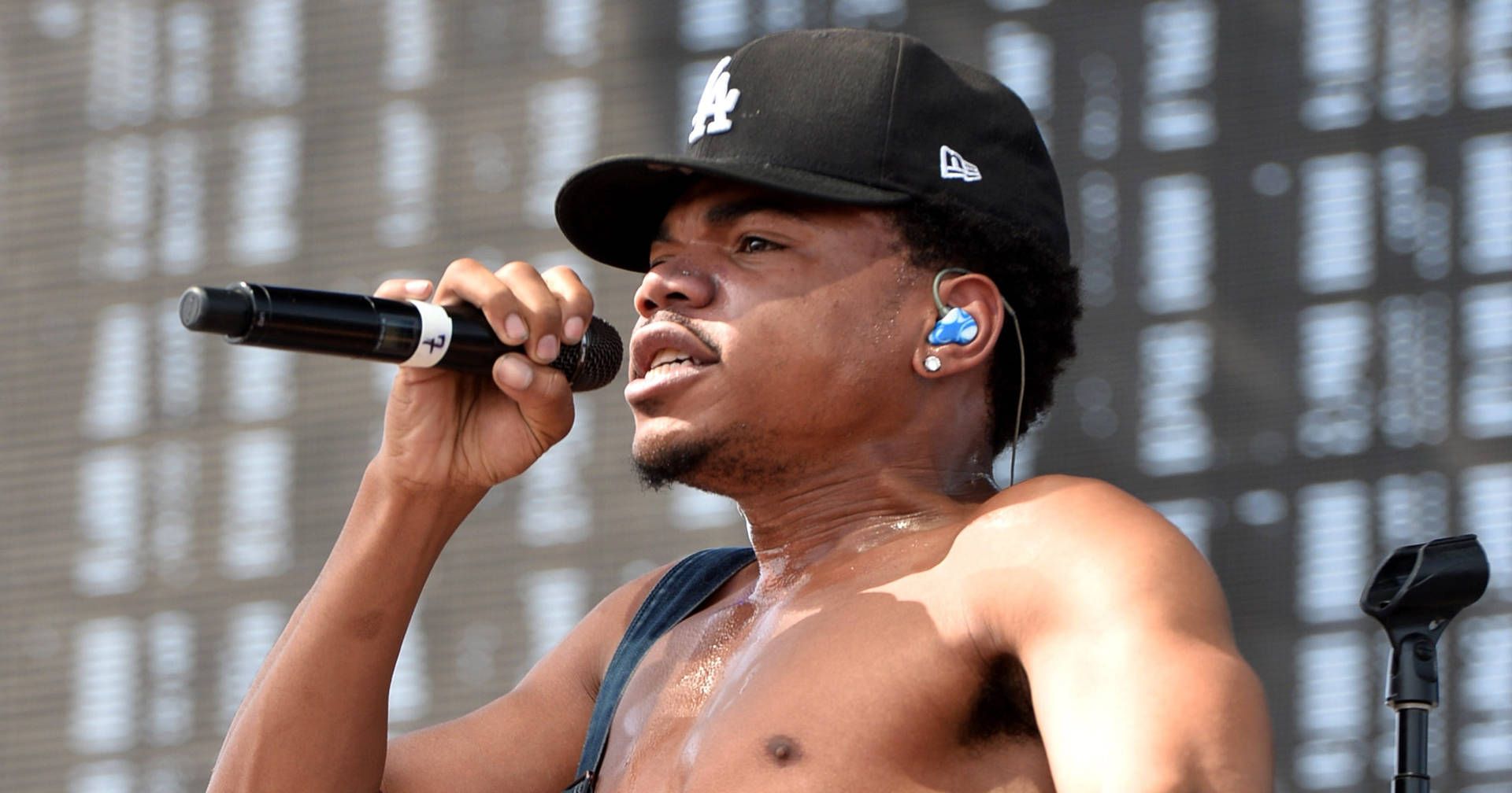 A man with no shirt on holding up his microphone - Chance the Rapper