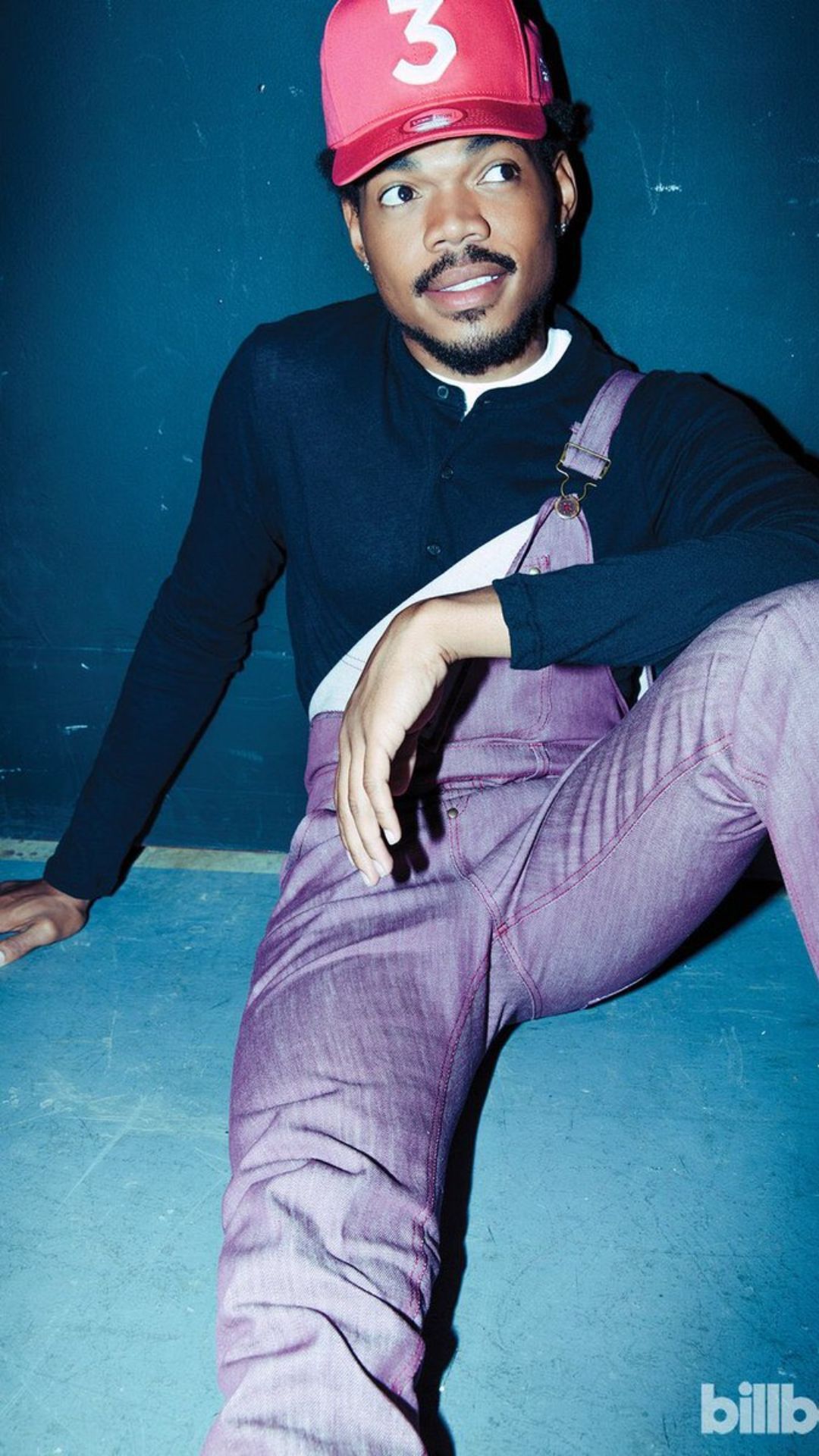 Rapper Chance the Rapper sitting on the ground wearing a red hat and purple pants. - Chance the Rapper