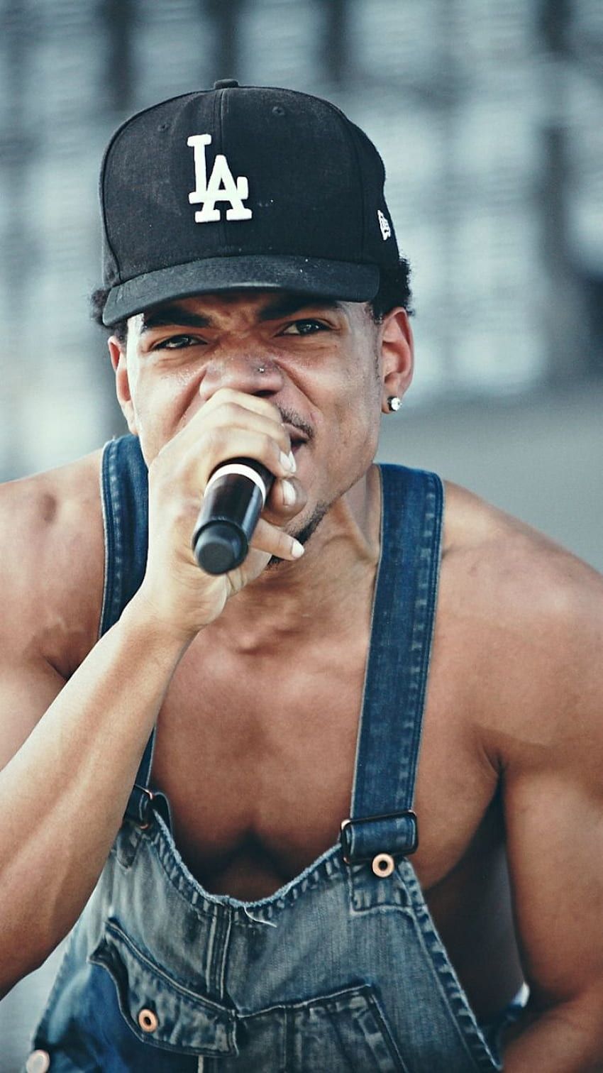 A man wearing an overalls and holding up his microphone - Chance the Rapper