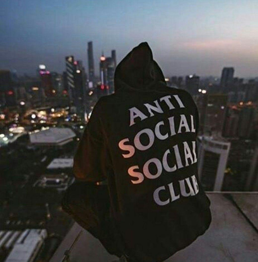 A man sitting on the edge of building with anti social club written across his back - Anti Social Social Club