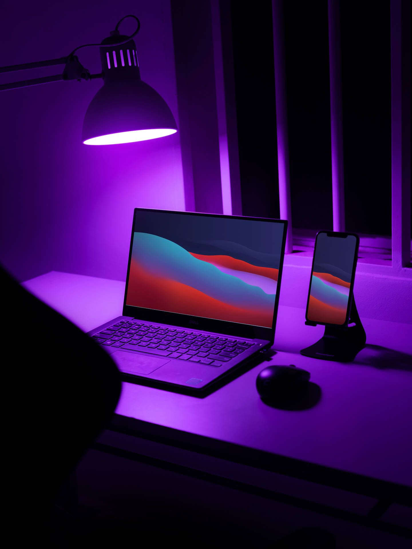 A laptop and phone sit on a desk under a purple light. - Technology