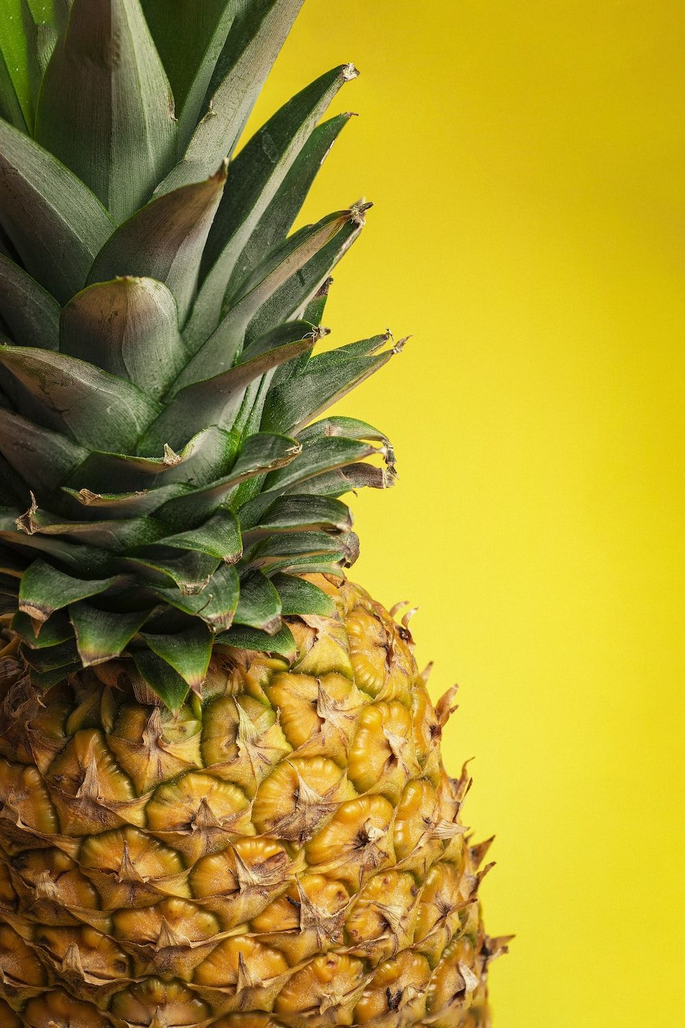 A pineapple is sitting on top of yellow background - Pineapple