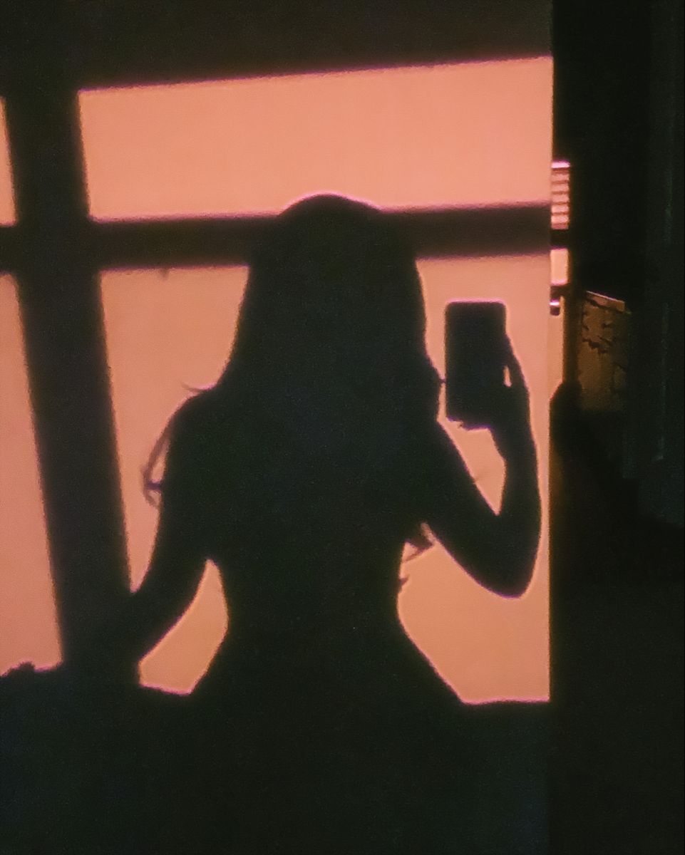 A woman's silhouette is seen in front of a window holding a phone. - Shadow