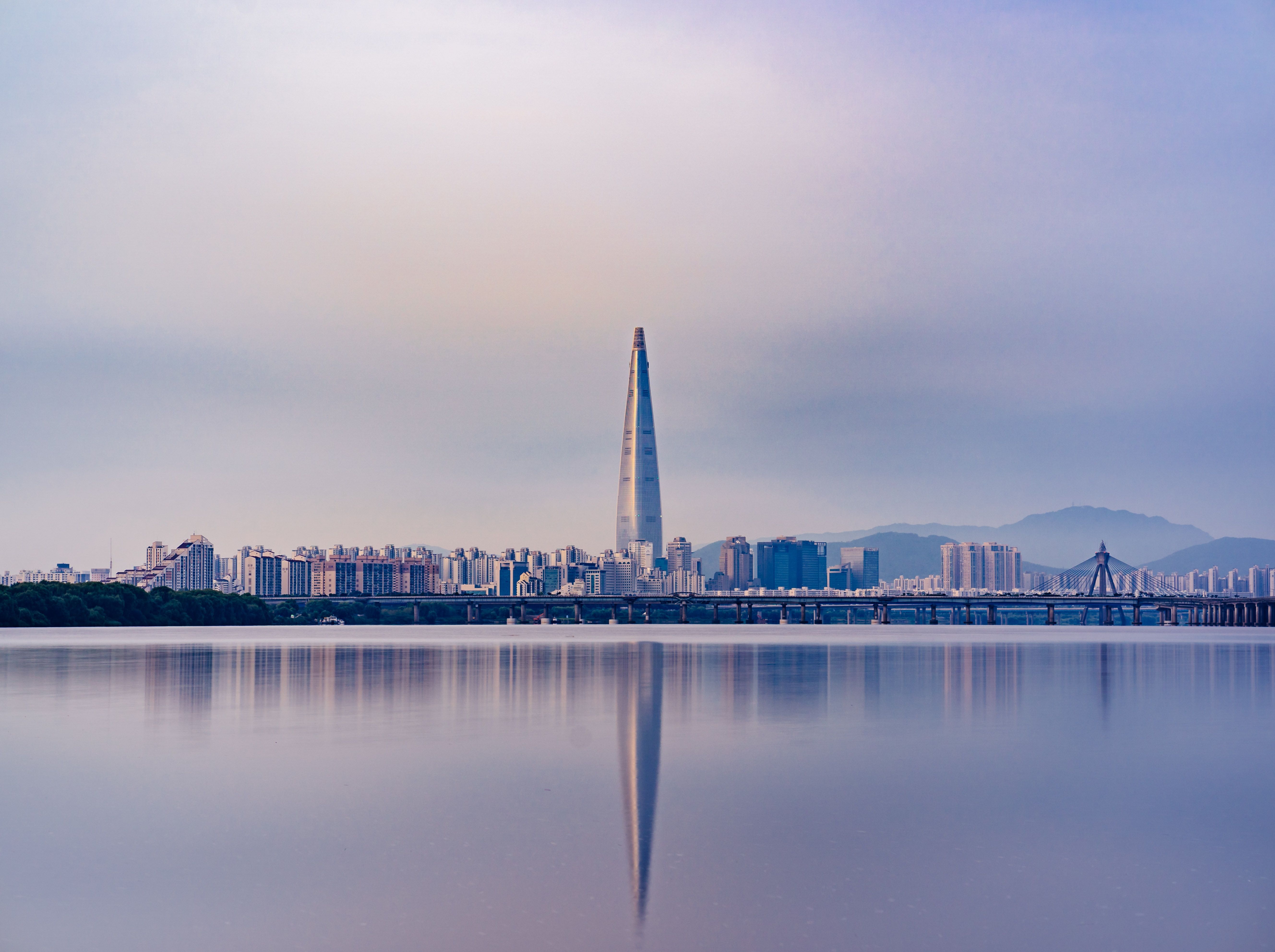 A city skyline with a tall building in the middle and a body of water in the foreground. - Seoul