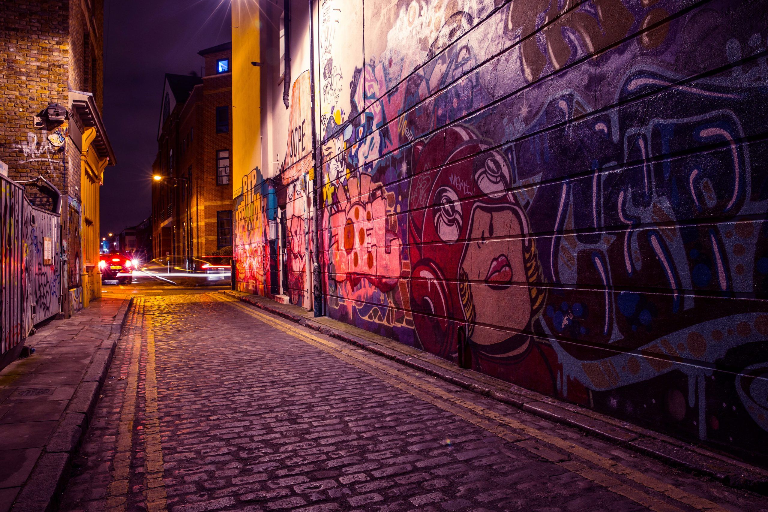 A street at night with a wall covered in graffiti - Street art