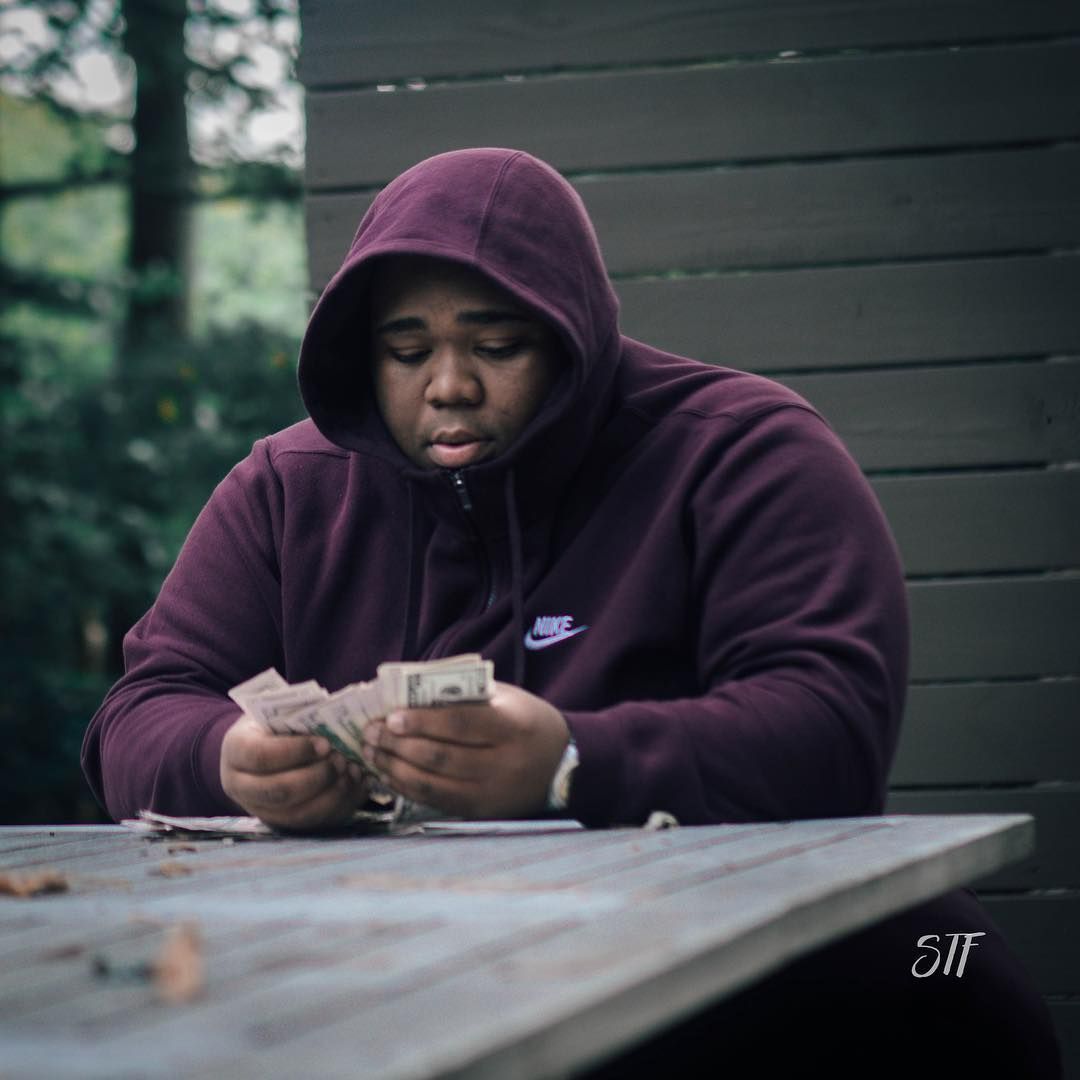 A man wearing a purple nike hoodie sitting at a table with money - Rod Wave