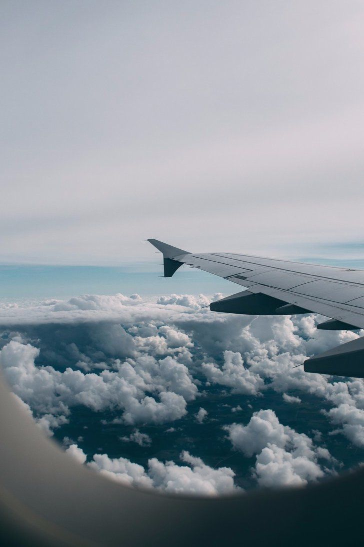 A wing of an airplane flying over clouds - Airplane