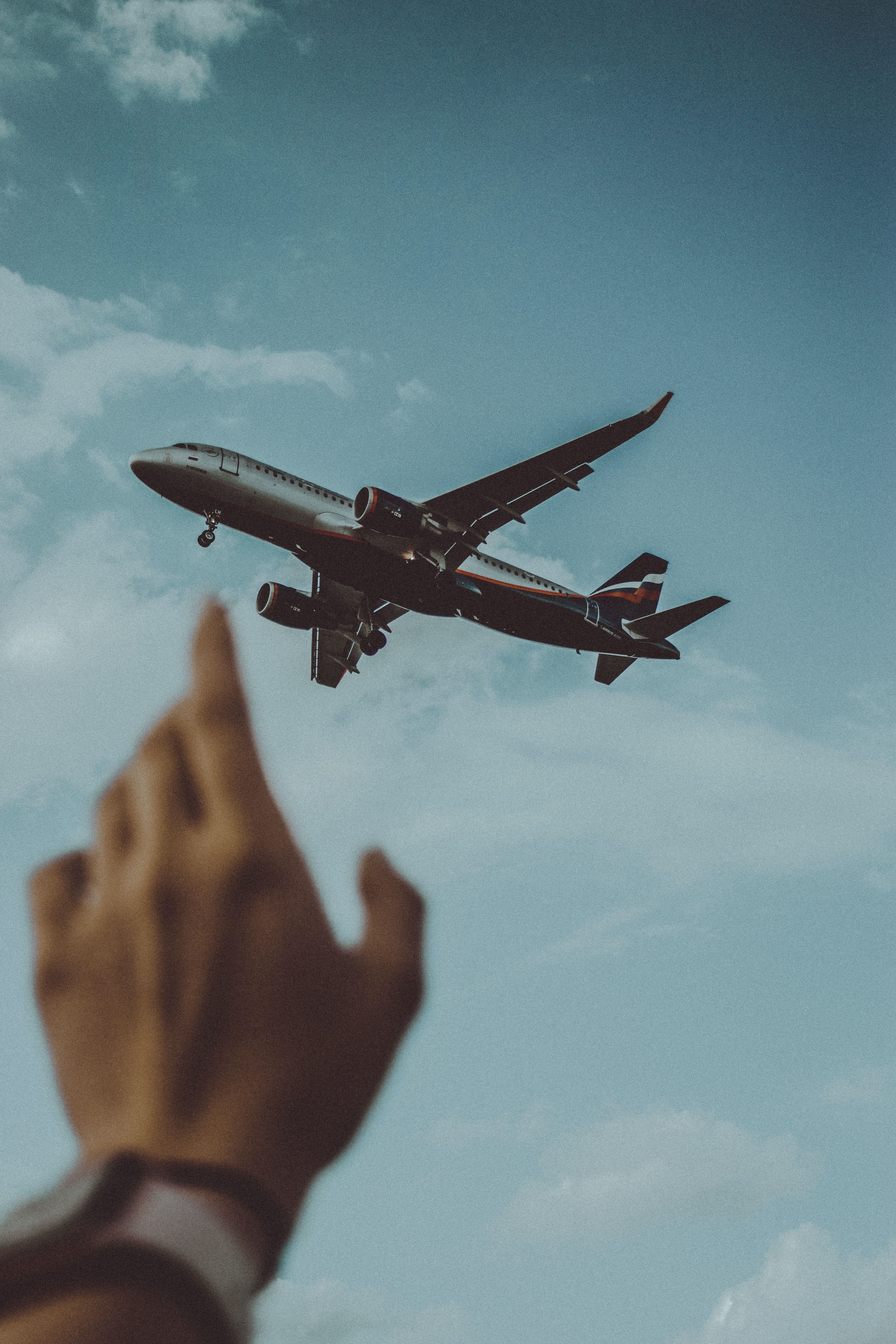 A hand pointing at an airplane flying in the sky - Airplane