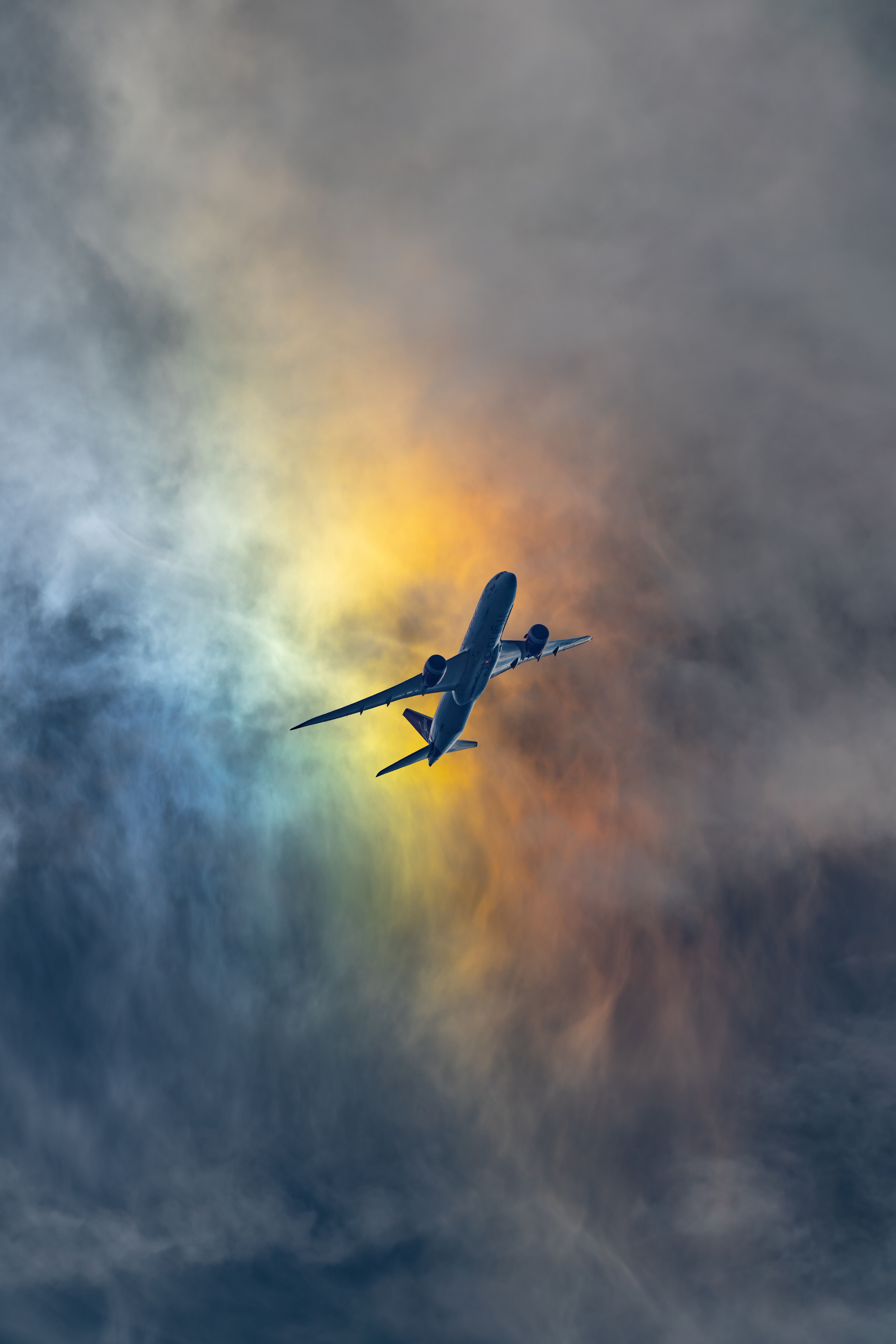 A plane flying through a cloudy sky with a rainbow behind it. - Airplane