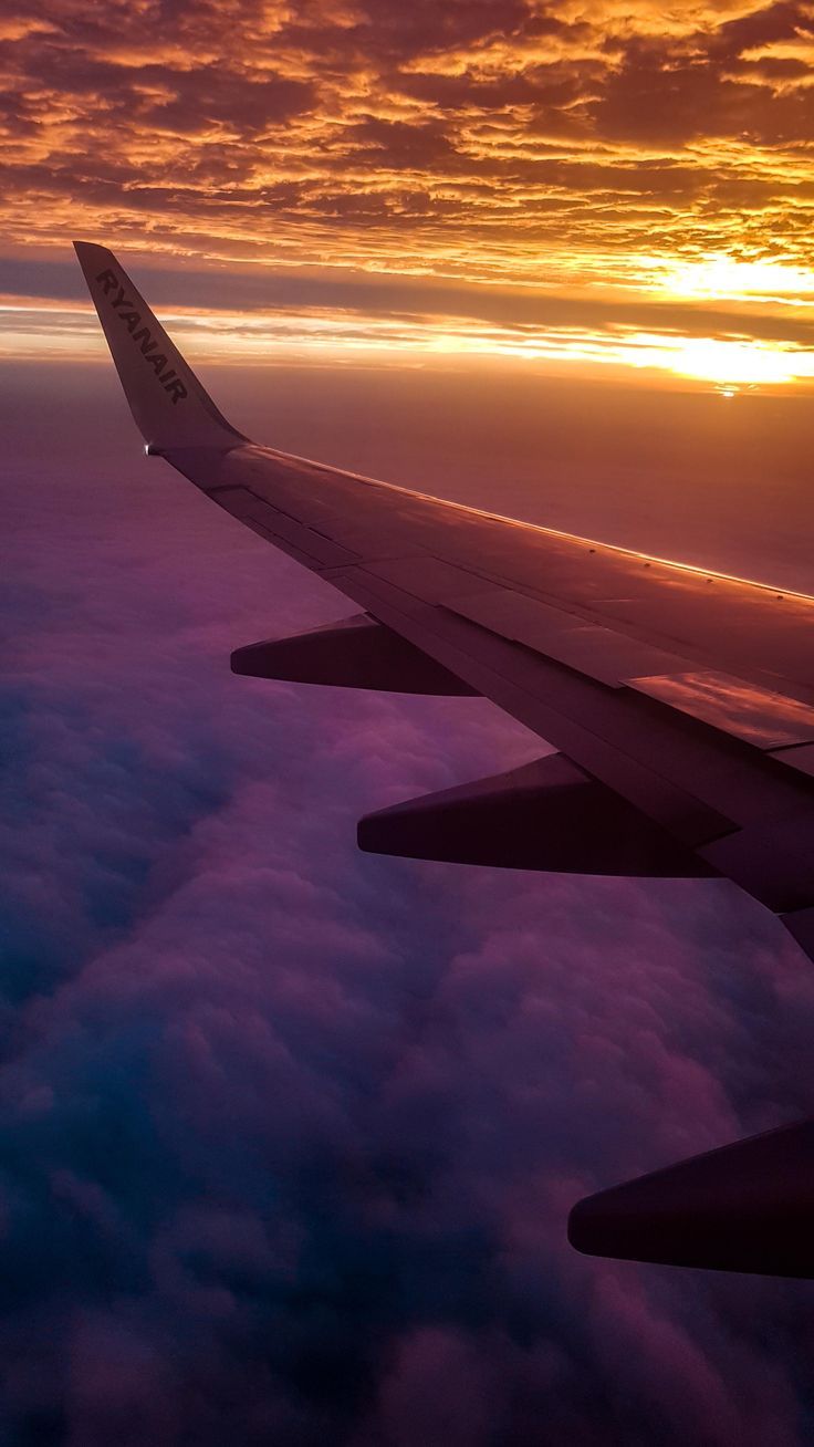 A wing of an airplane flying over clouds - Airplane