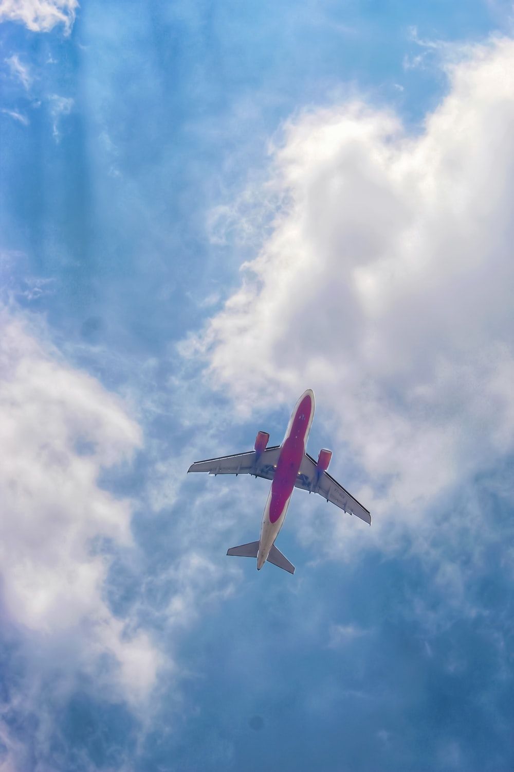 A pink and white airplane flying through a cloudy blue sky. - Airplane