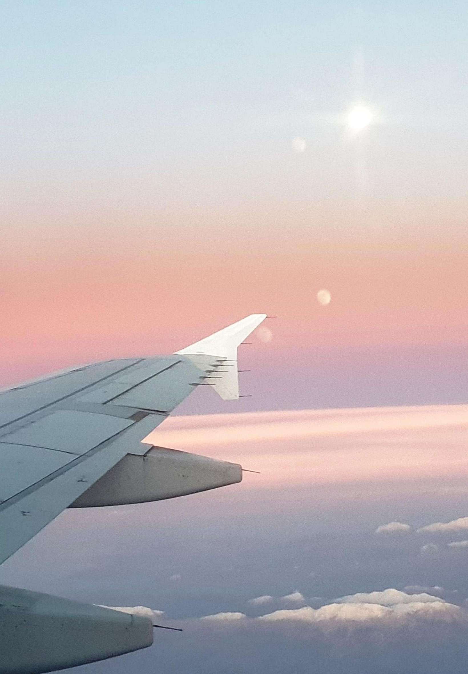 A plane wing is seen in front of a cloudy sky during sunset. - Airplane