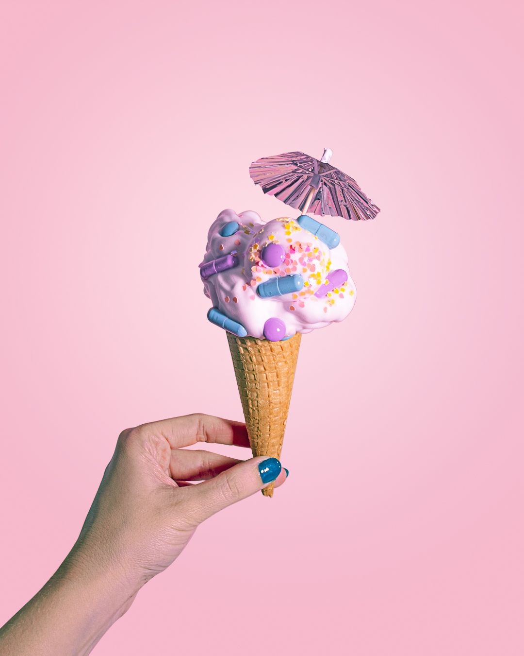 A hand holding a cone with a colorful ice cream and a pink umbrella on a pink background - Ice cream