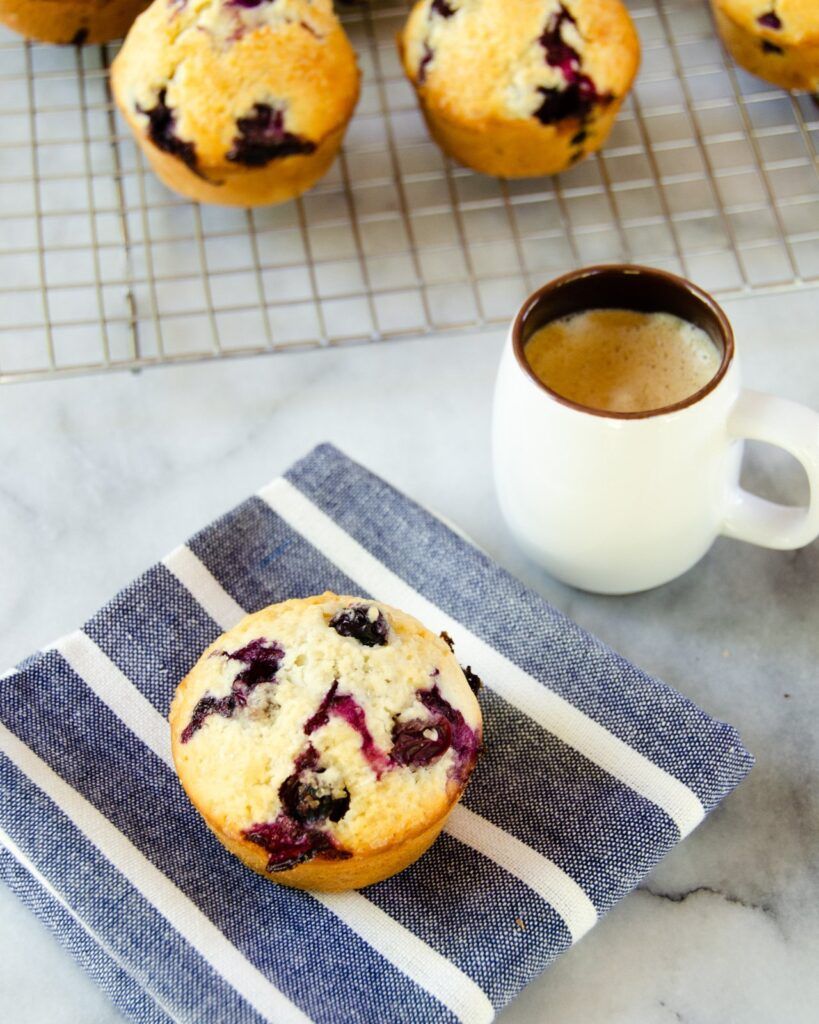 Blueberry muffin on a blue and white striped napkin with a cup of coffee. - 