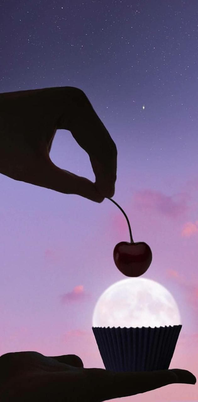 A hand placing a cherry on top of a cupcake with the moon as the cupcake - 