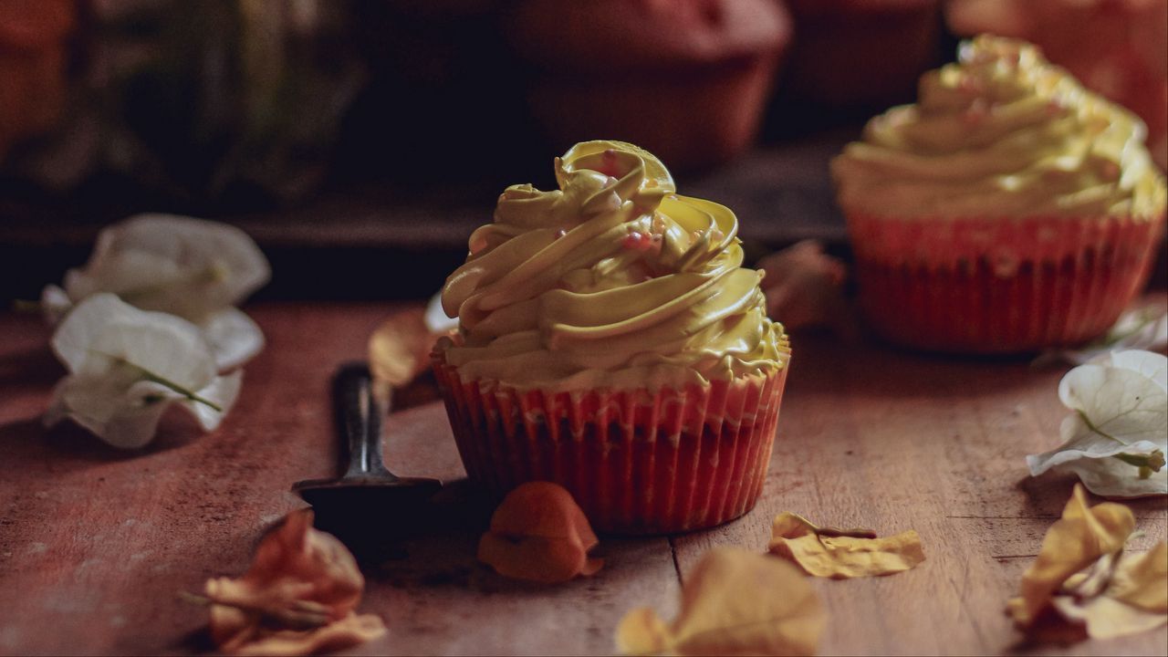 A cupcake with yellow frosting on a wooden table. - 