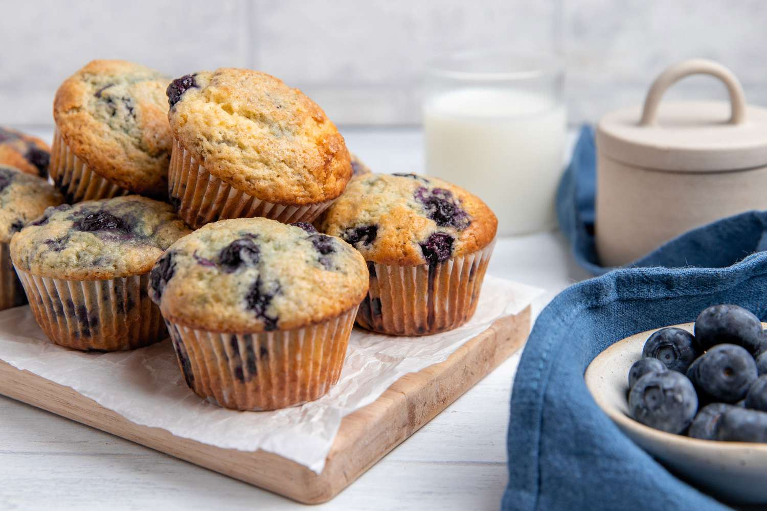 A wooden board with blueberry muffins and bowls of berries - 