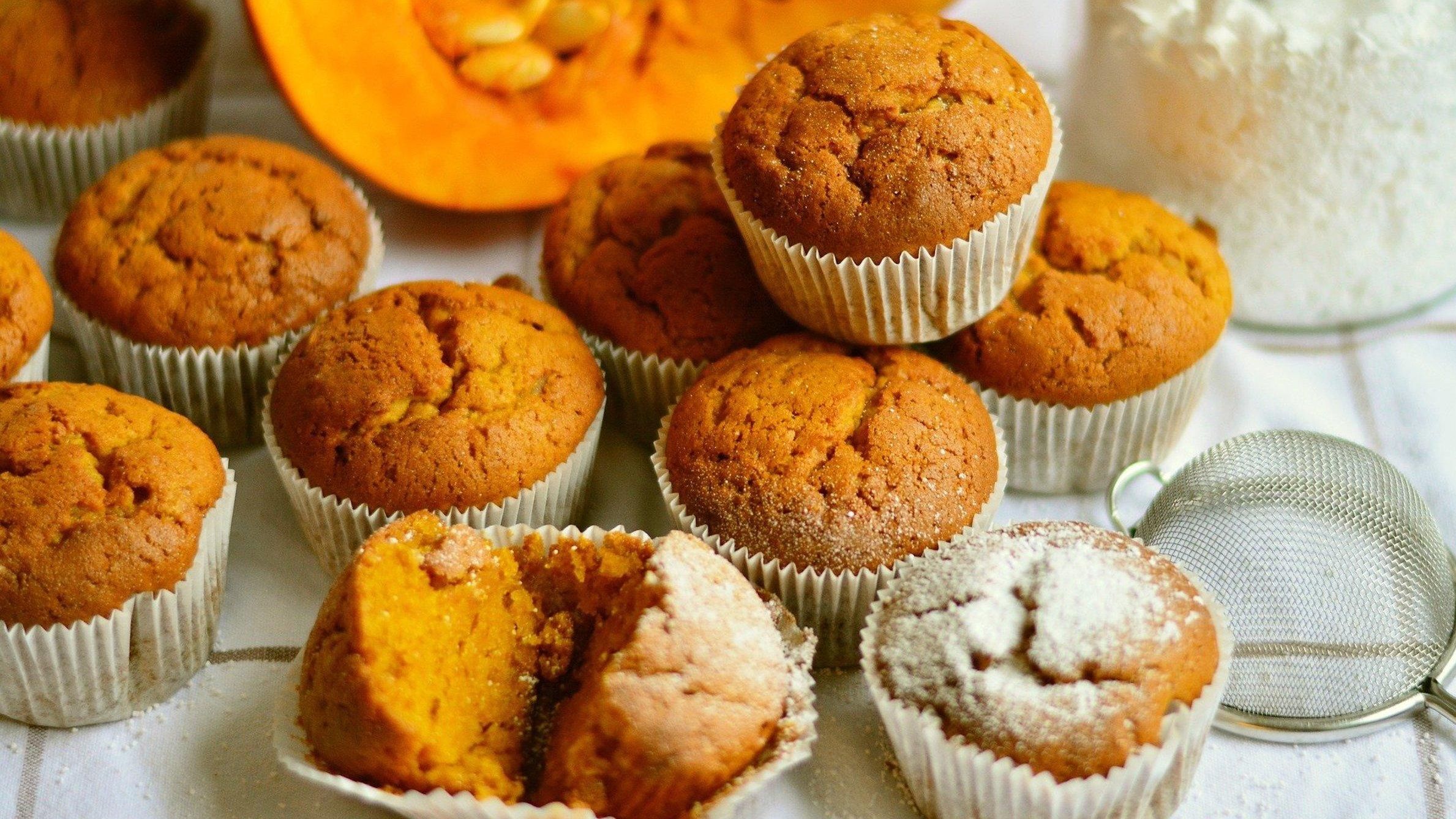 A plate of muffins with one of them cut in half to show the pumpkin inside. - 