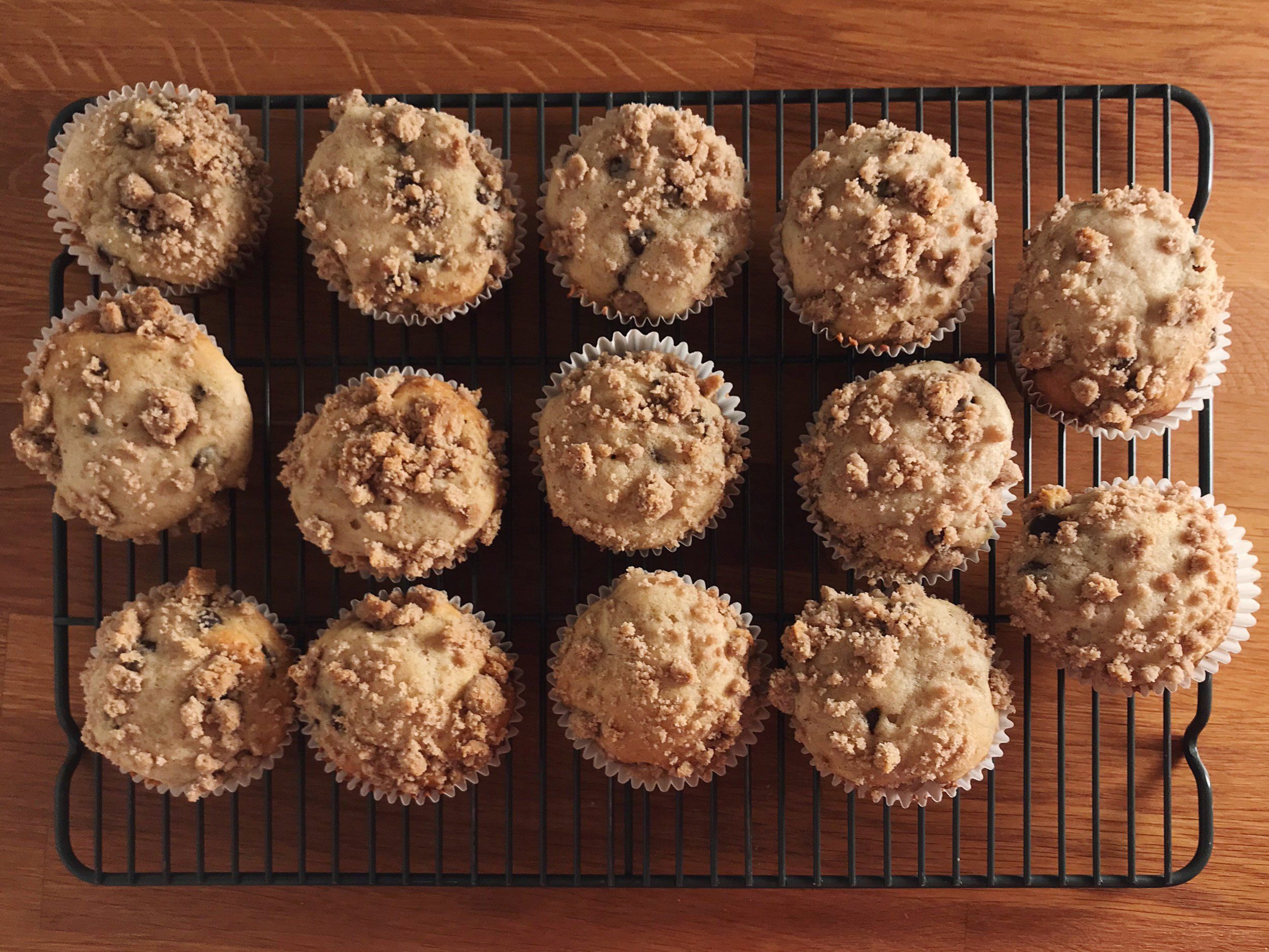 Cooling rack of blueberry muffins with crumb topping on a wooden table. - 