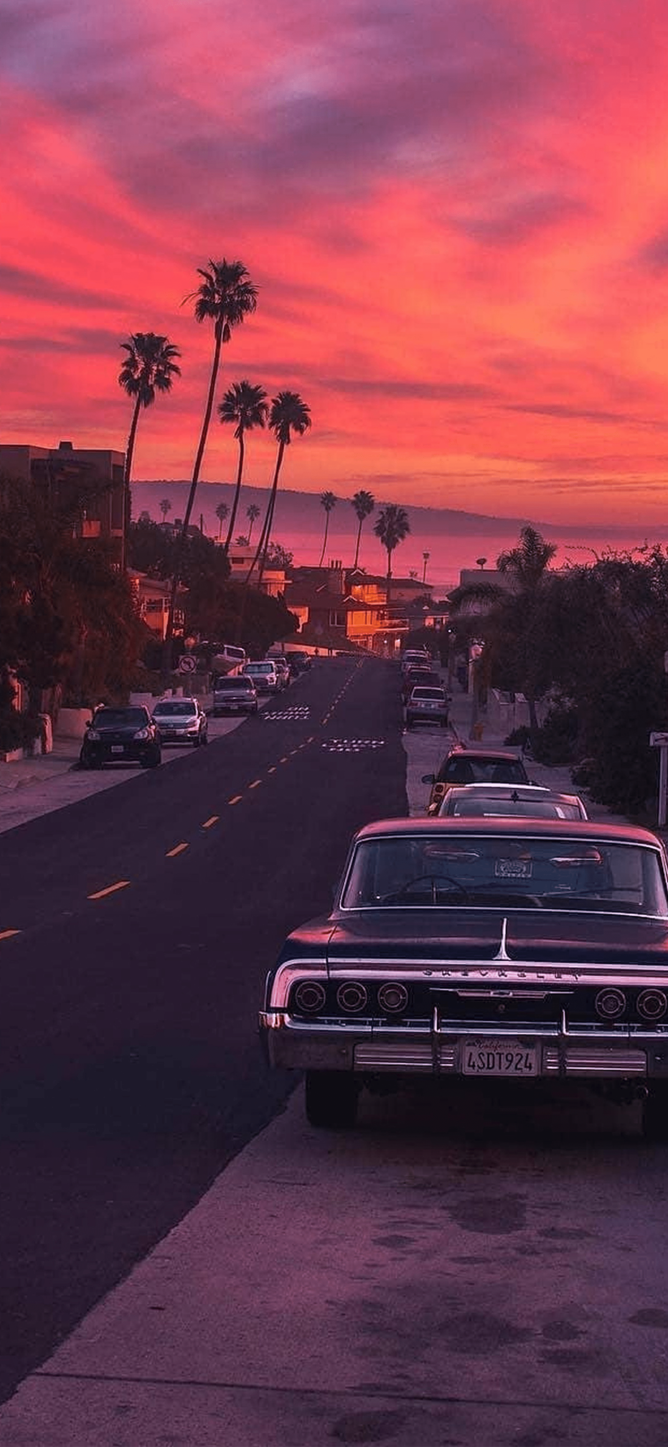 A vintage car parked on the side of the road with a sunset in the background. - Cars