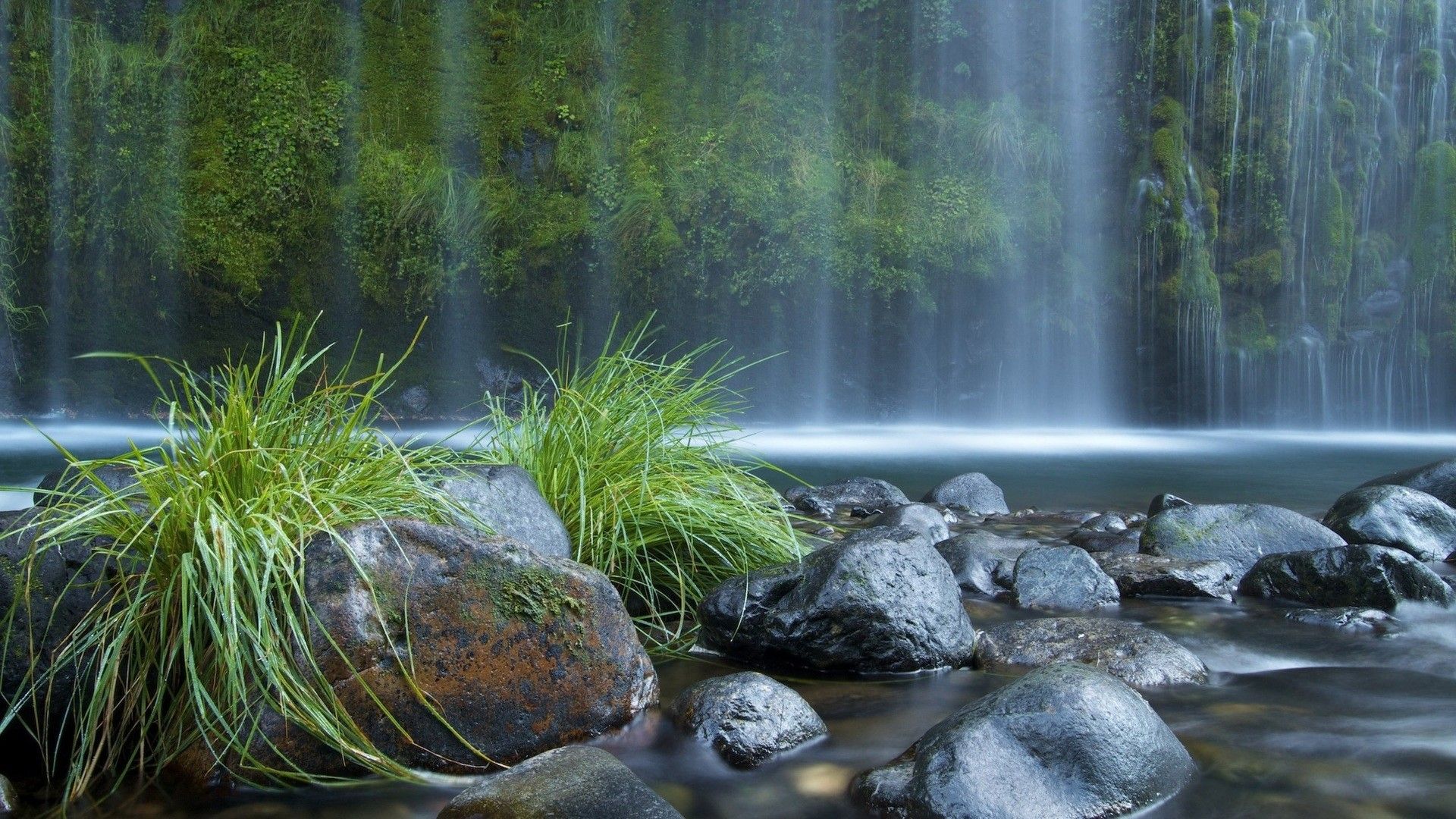 A waterfall is flowing over rocks and grass - Waterfall