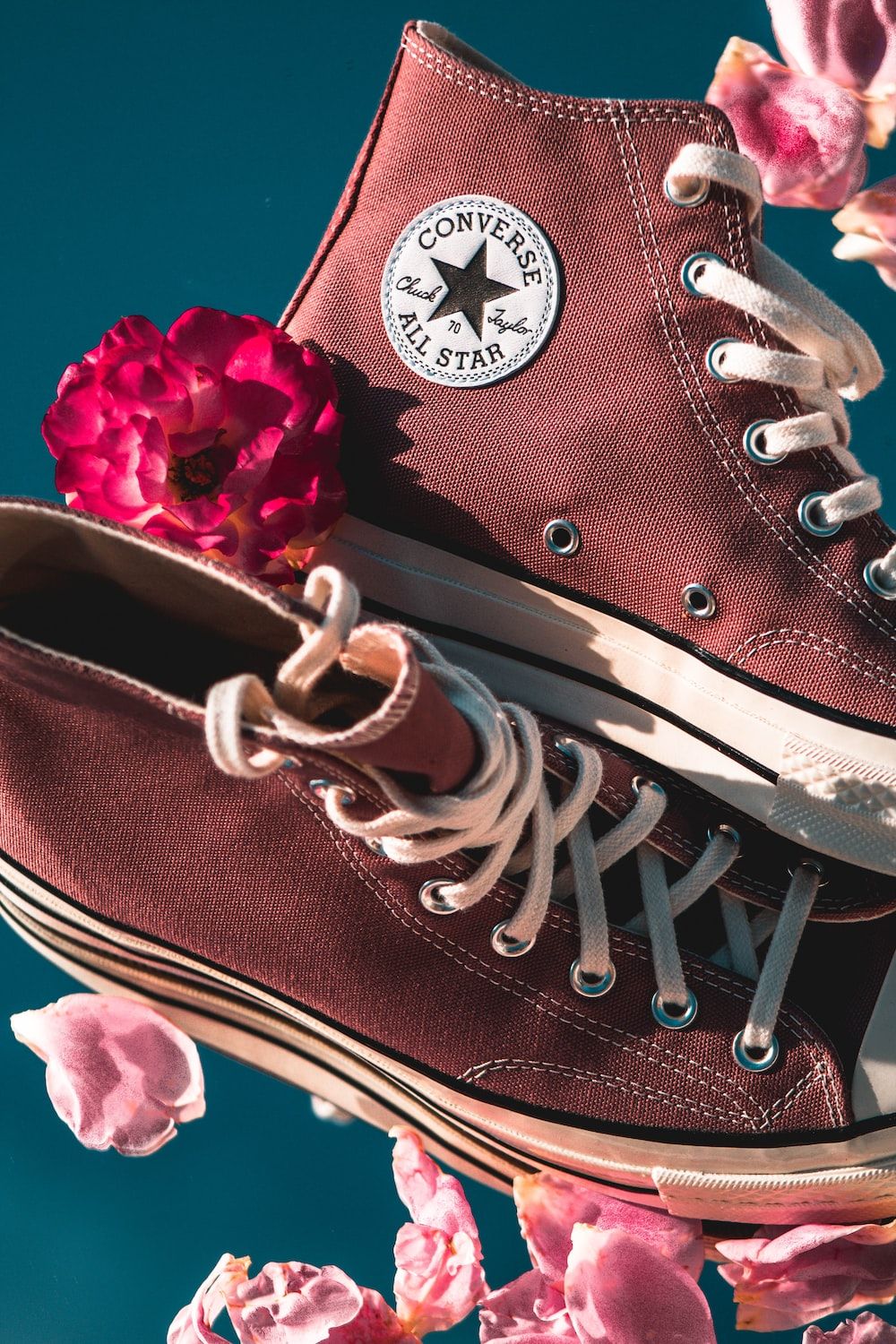 A pair of converse shoes sitting on top flowers - Converse