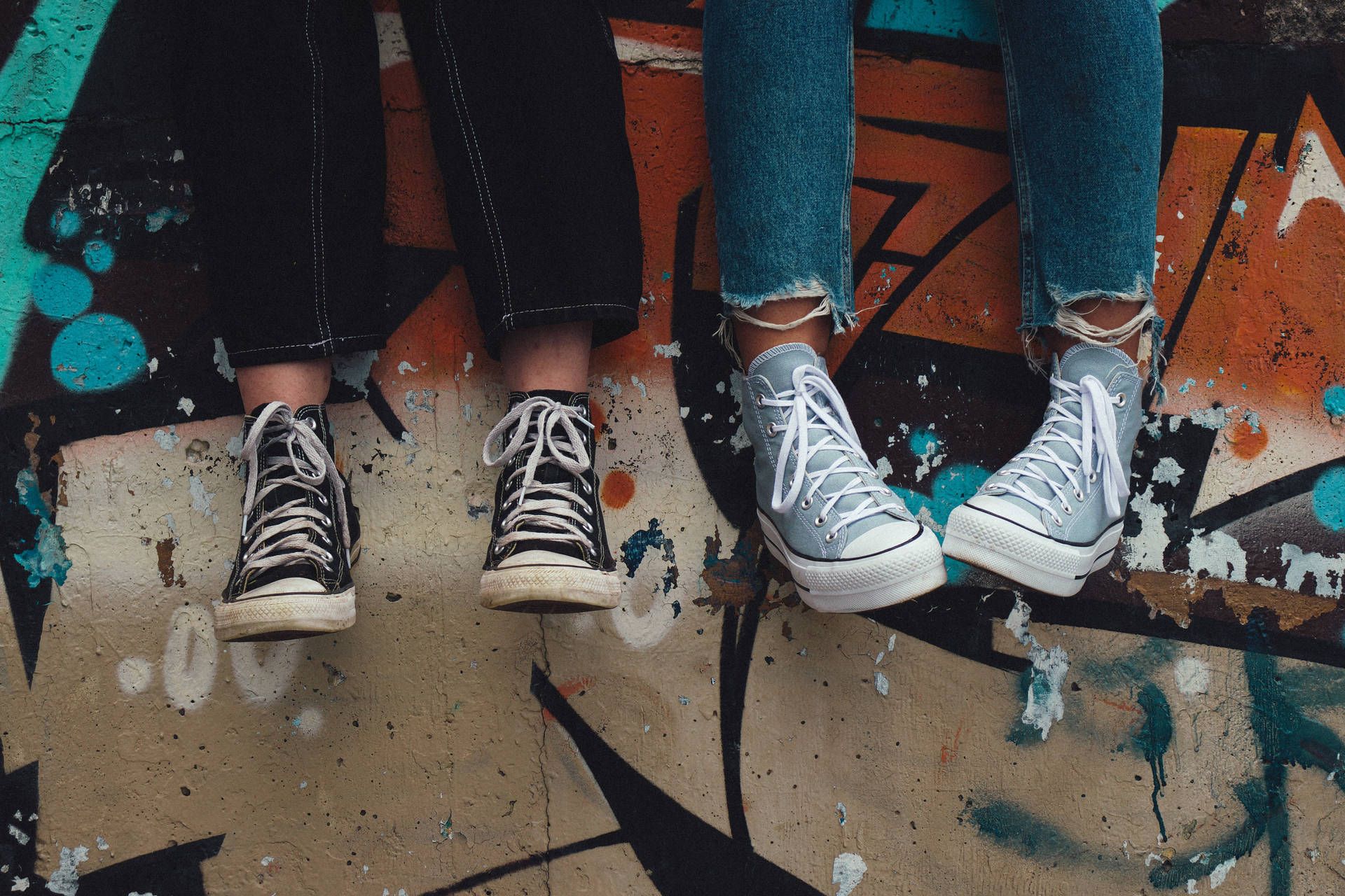 Two people are sitting on a wall with their shoes - Converse