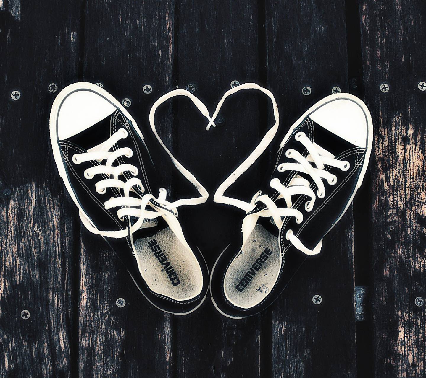 A pair of black Converse sneakers with white laces, the laces are tied in a heart shape. - Converse