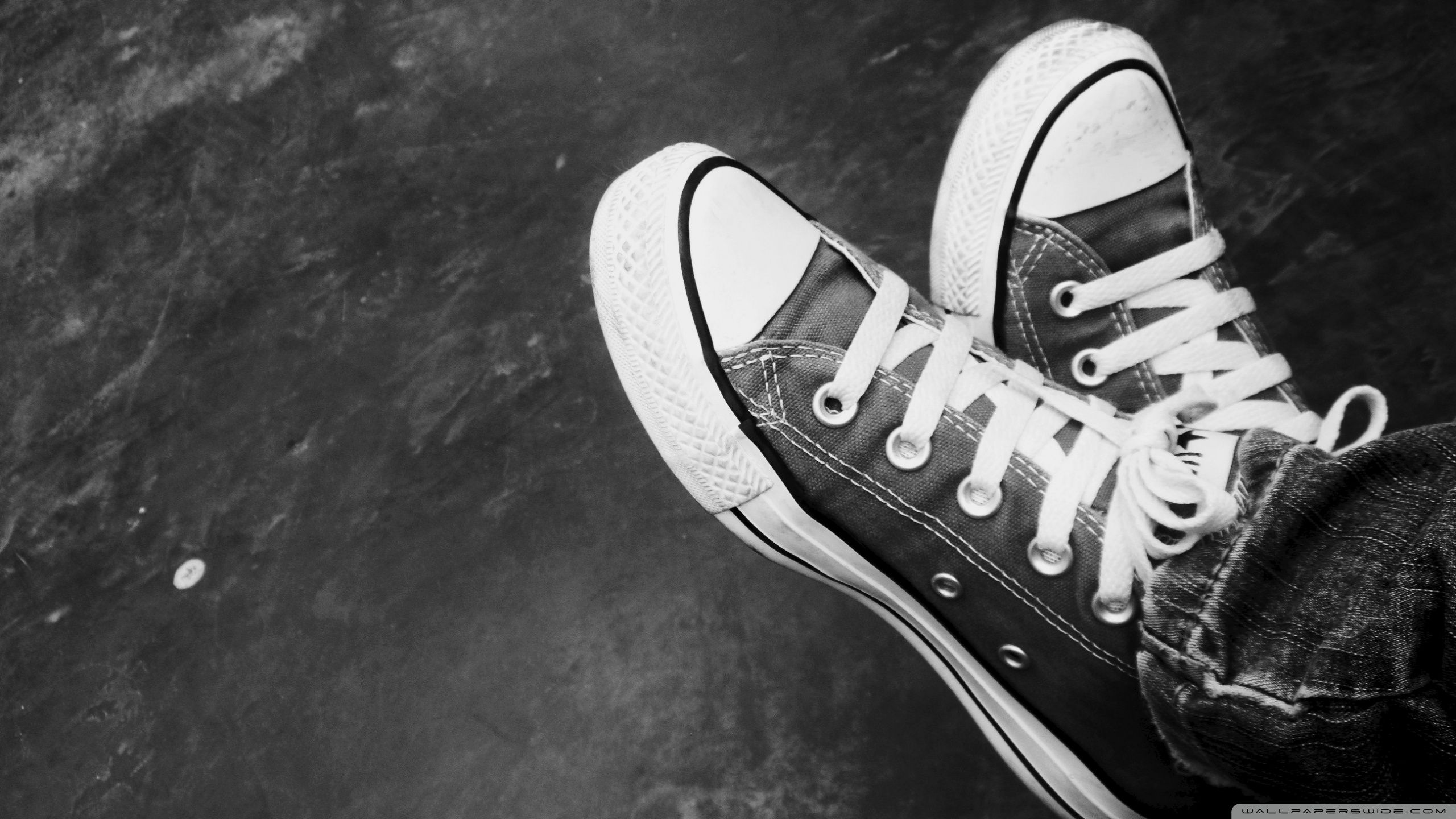 A black and white photo of someone's feet wearing converse shoes - Converse