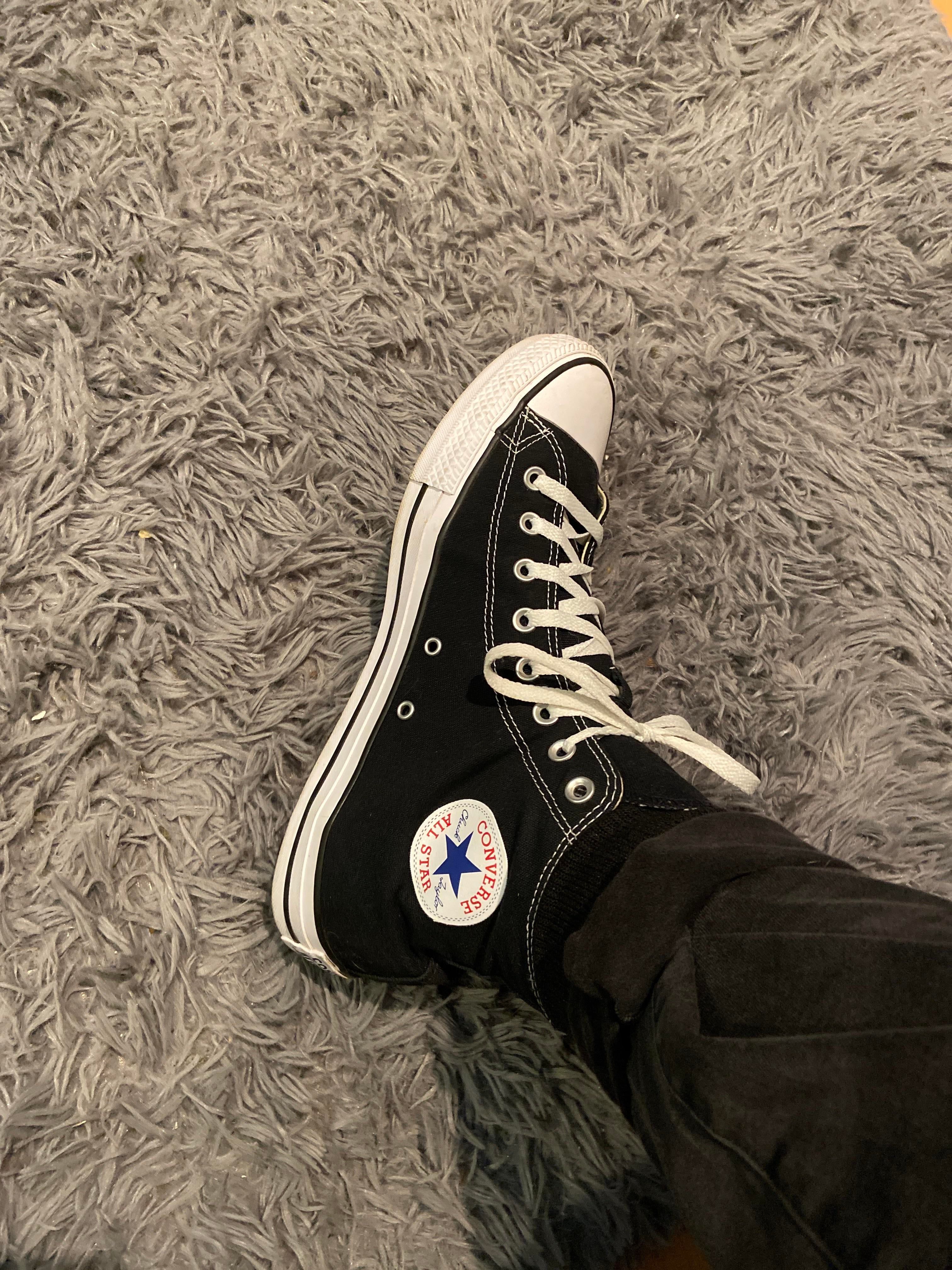 A person wearing black converse shoes on top of some carpet - Converse