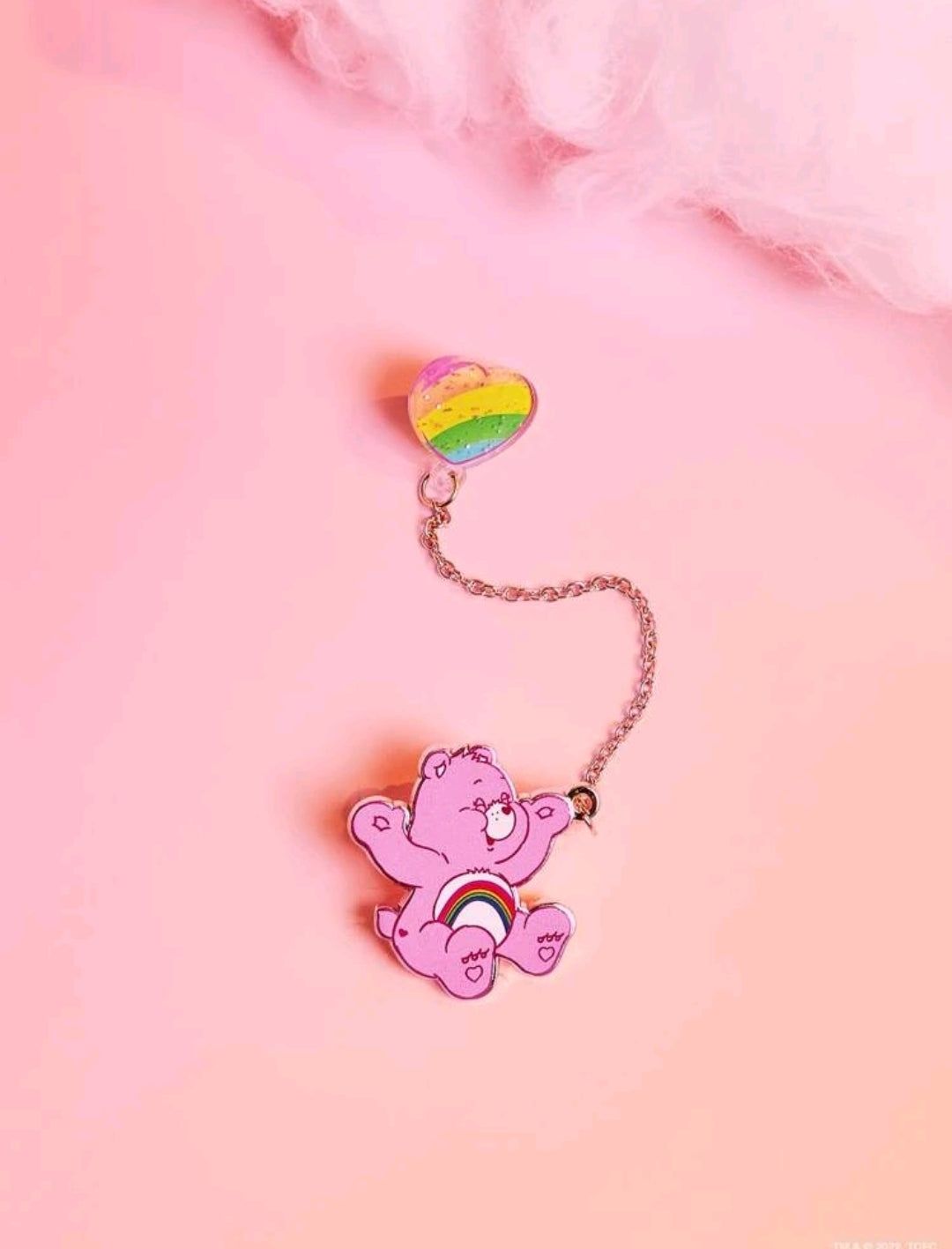 A Care Bear enamel pin in pink with a rainbow heart. - Care Bears