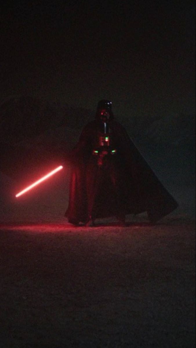 Darth Vader standing in the dark with his red lightsaber lit up - Darth Vader