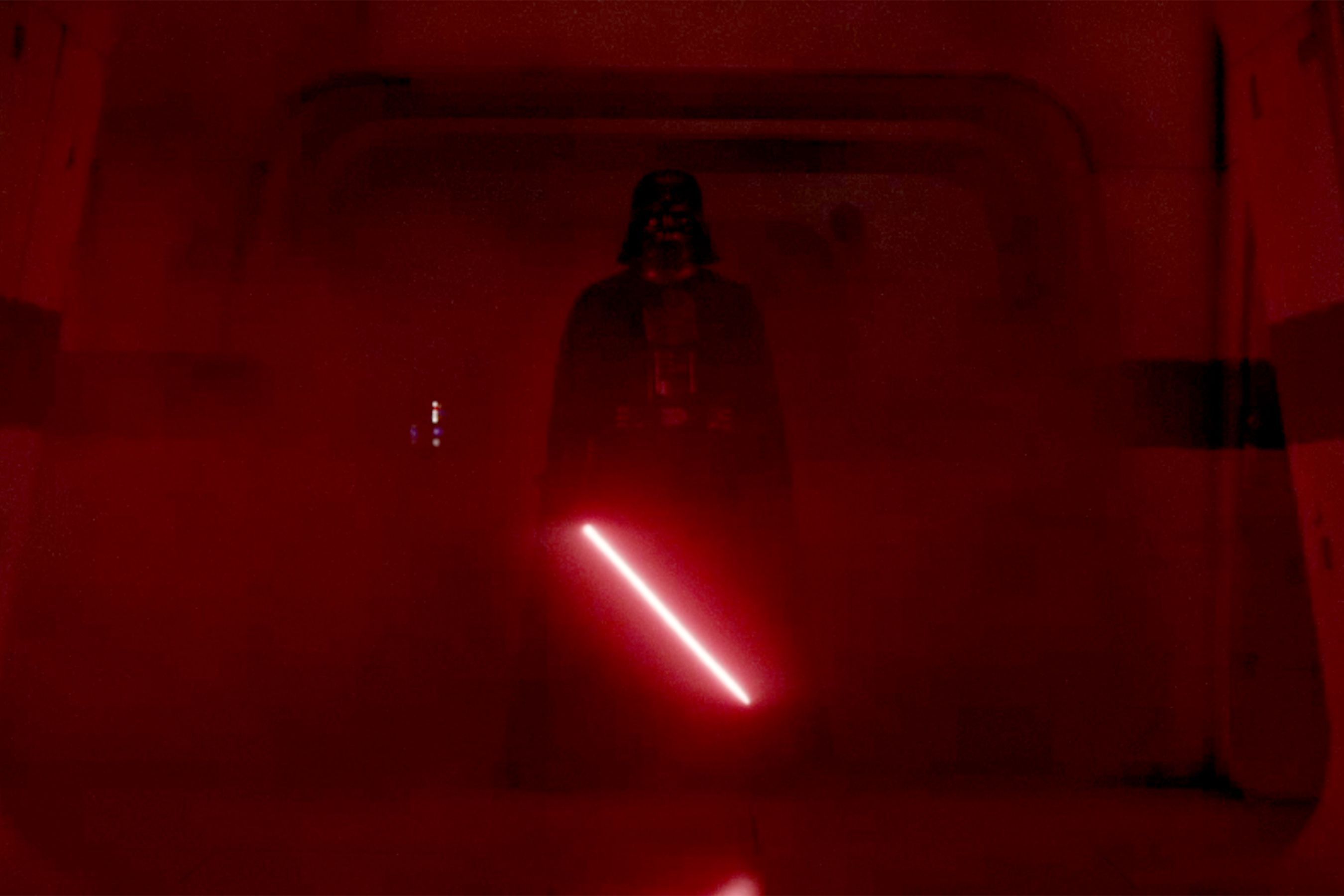 Darth Vader standing in a red-lit hallway with his red lightsaber lit - Darth Vader