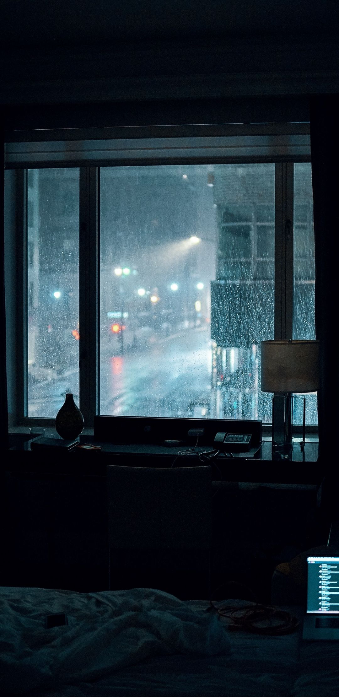 A room with a desk and a window with a view of a rainy city street - Rain