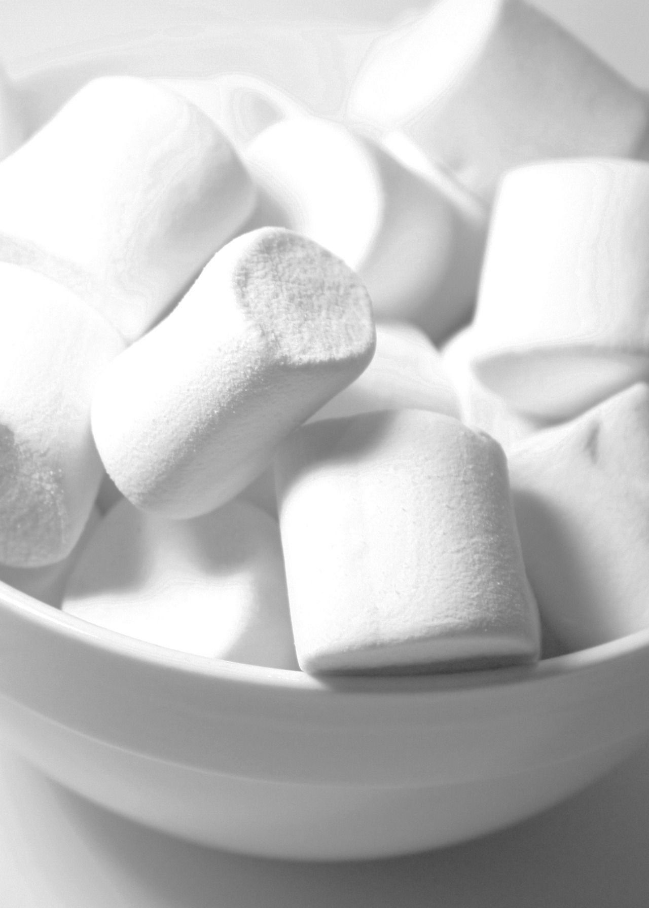 A bowl of marshmallows, with a few scattered on the table. - Marshmallows