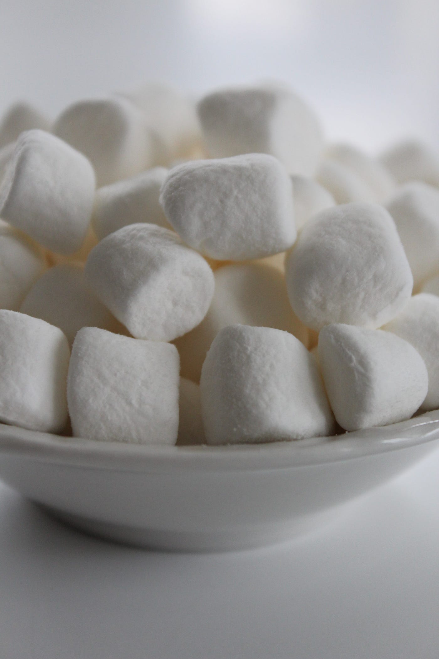 A bowl of white marshmallows on a white table. - Marshmallows
