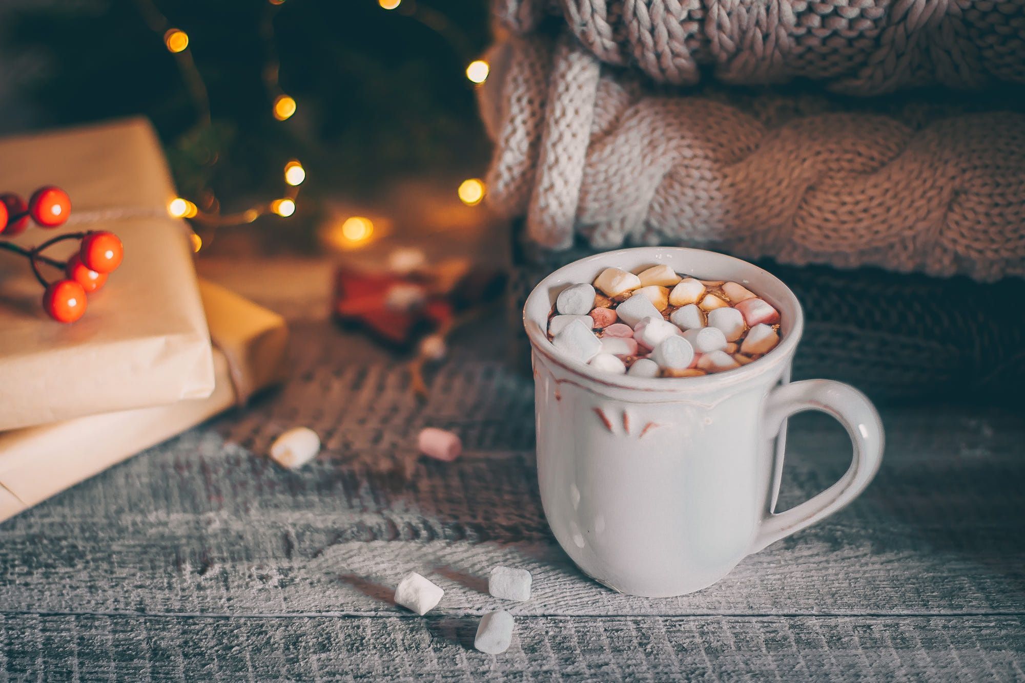 A white mug of hot chocolate with marshmallows, surrounded by a stack of books and a warm sweater. - Marshmallows, chocolate