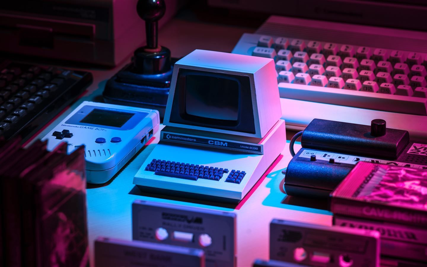 A collection of old computer hardware, including a keyboard, monitor, and game console, is lit up in blue and pink light. - 1440x900