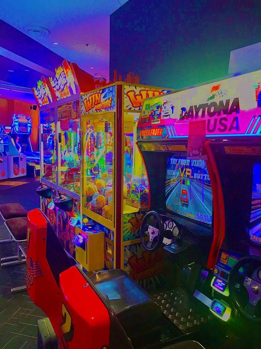 The interior of an arcade with a variety of games and neon lights. - Arcade