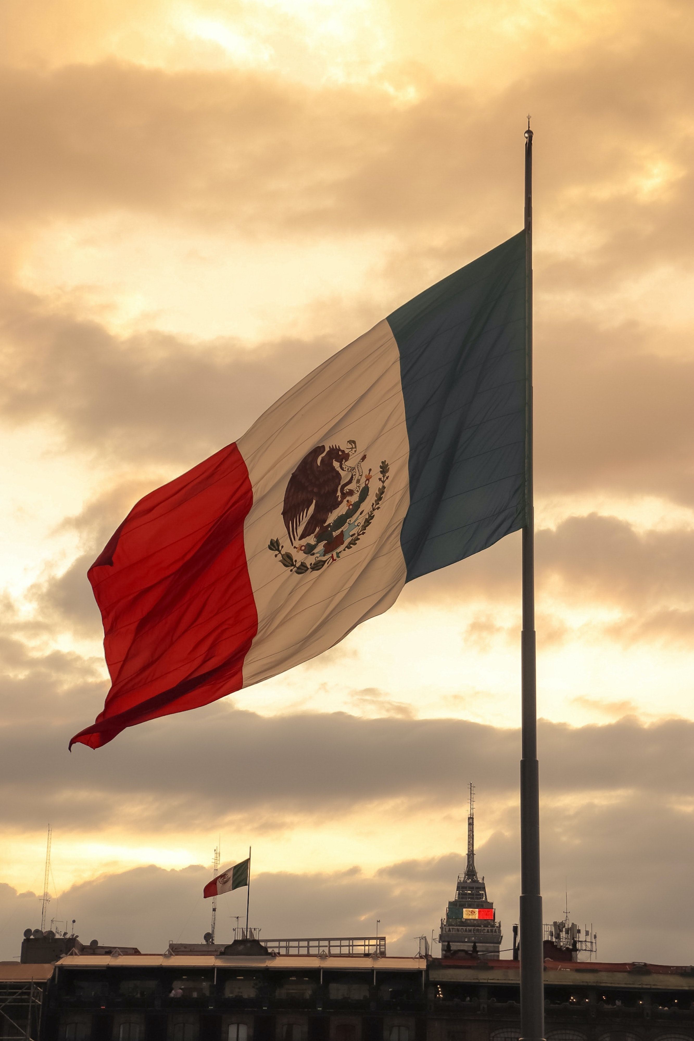 A Mexican flag waves in the wind in front of a cloudy sky. - Mexico