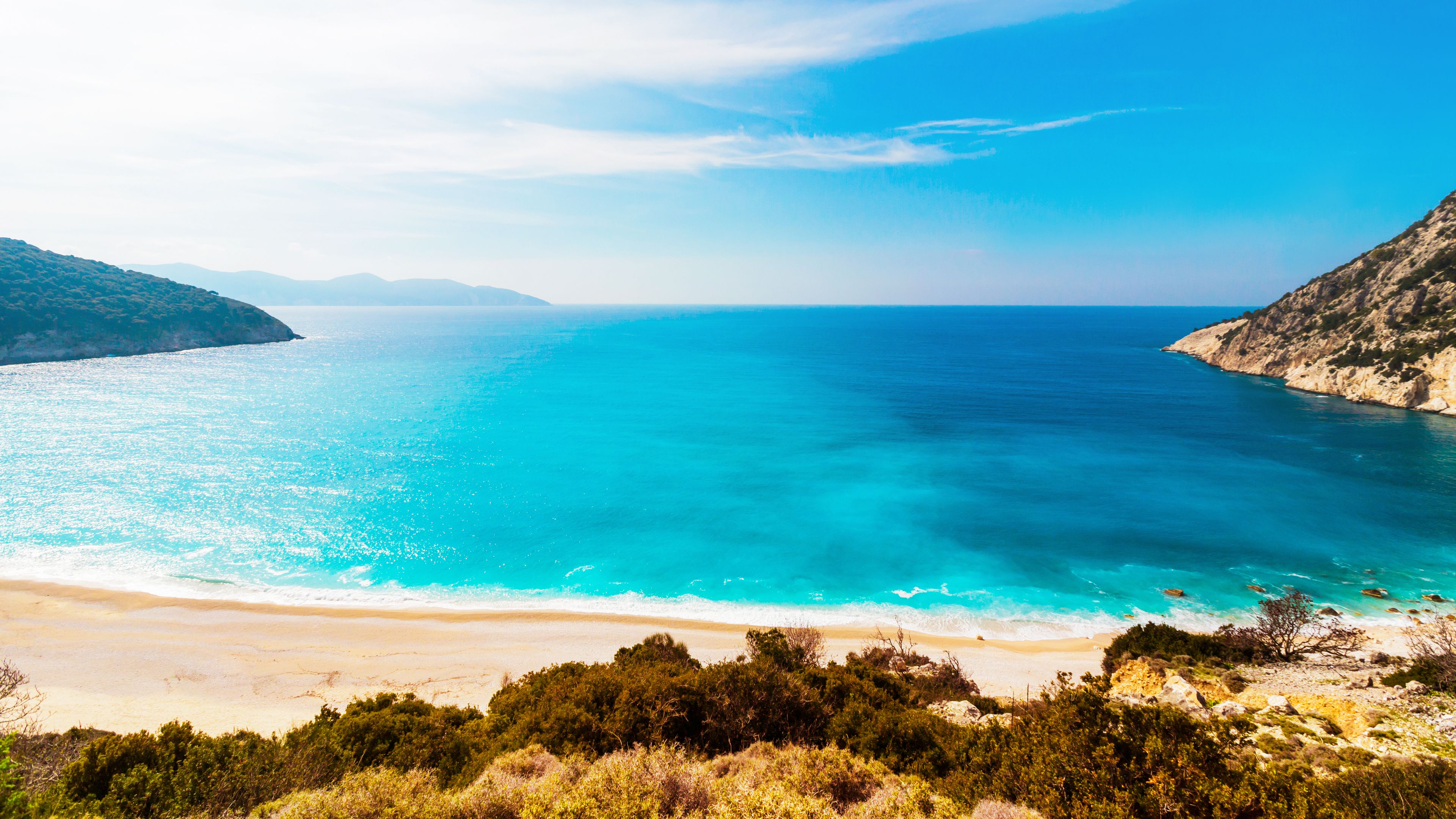 A beach with water and mountains in the background - Ocean
