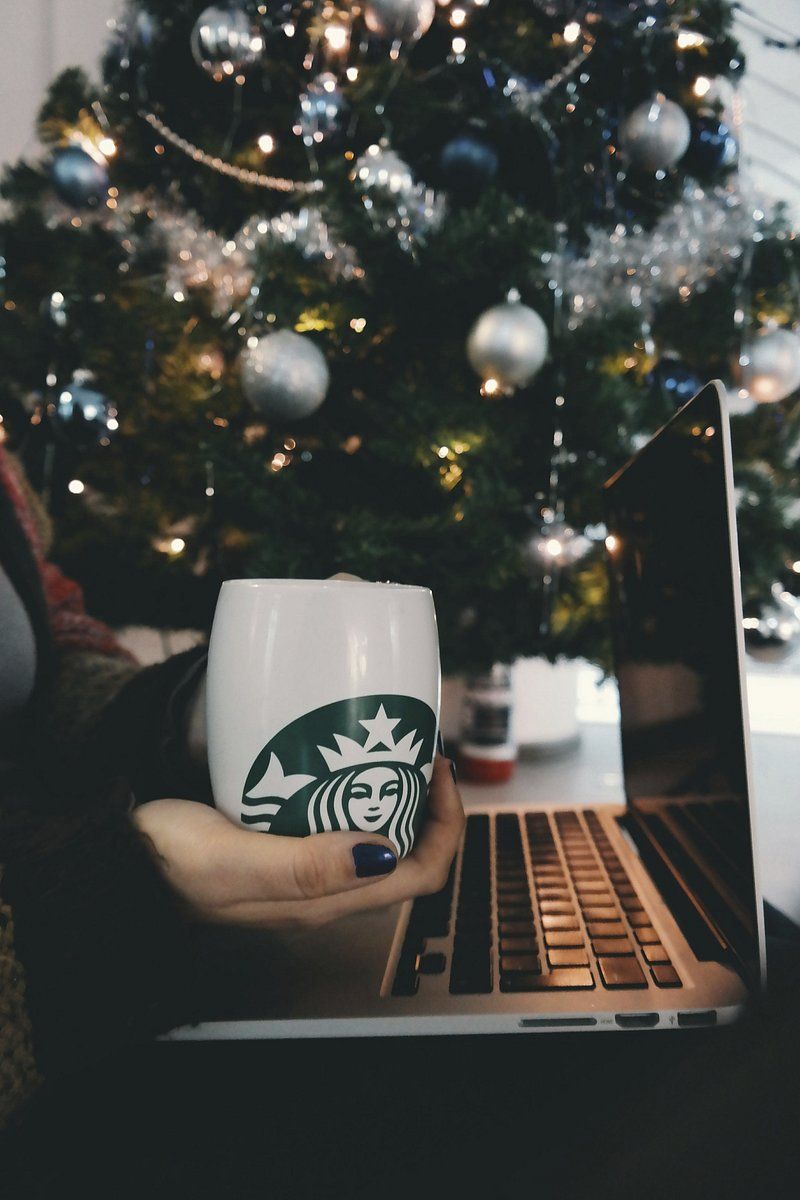 A person holding a Starbucks cup in front of a laptop. - Starbucks