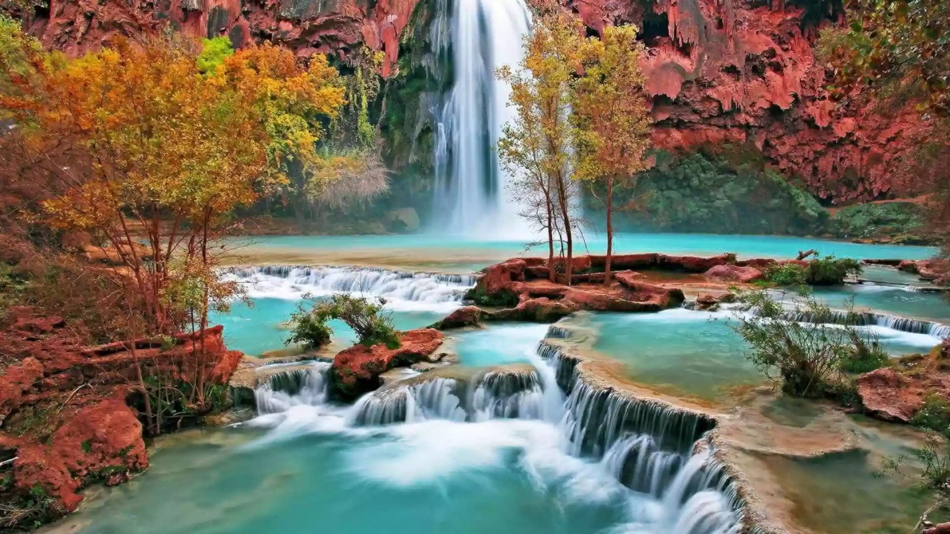 A waterfall surrounded by red rocks and trees. - River