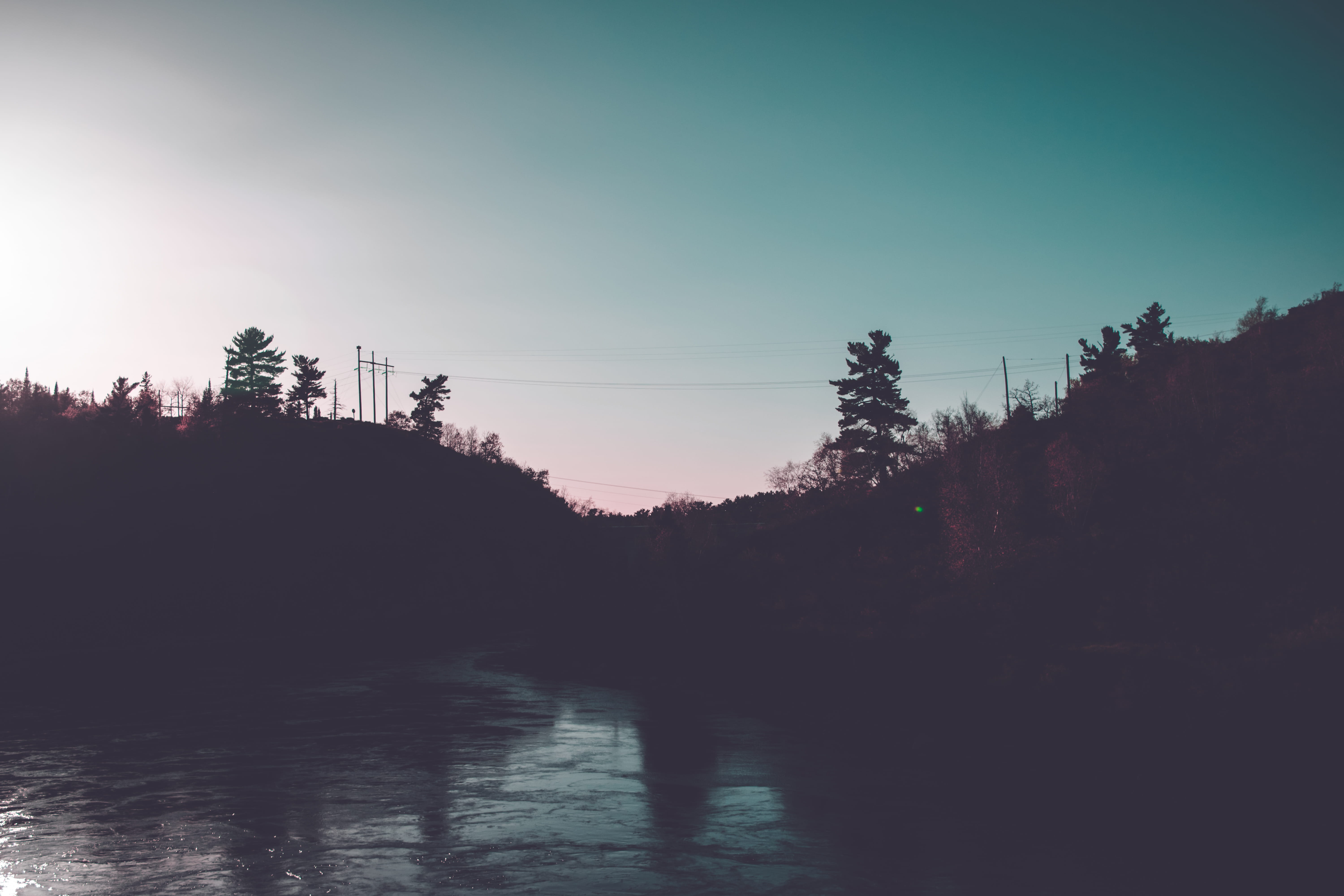 A body of water surrounded by trees with a blue and purple sunset in the background. - River