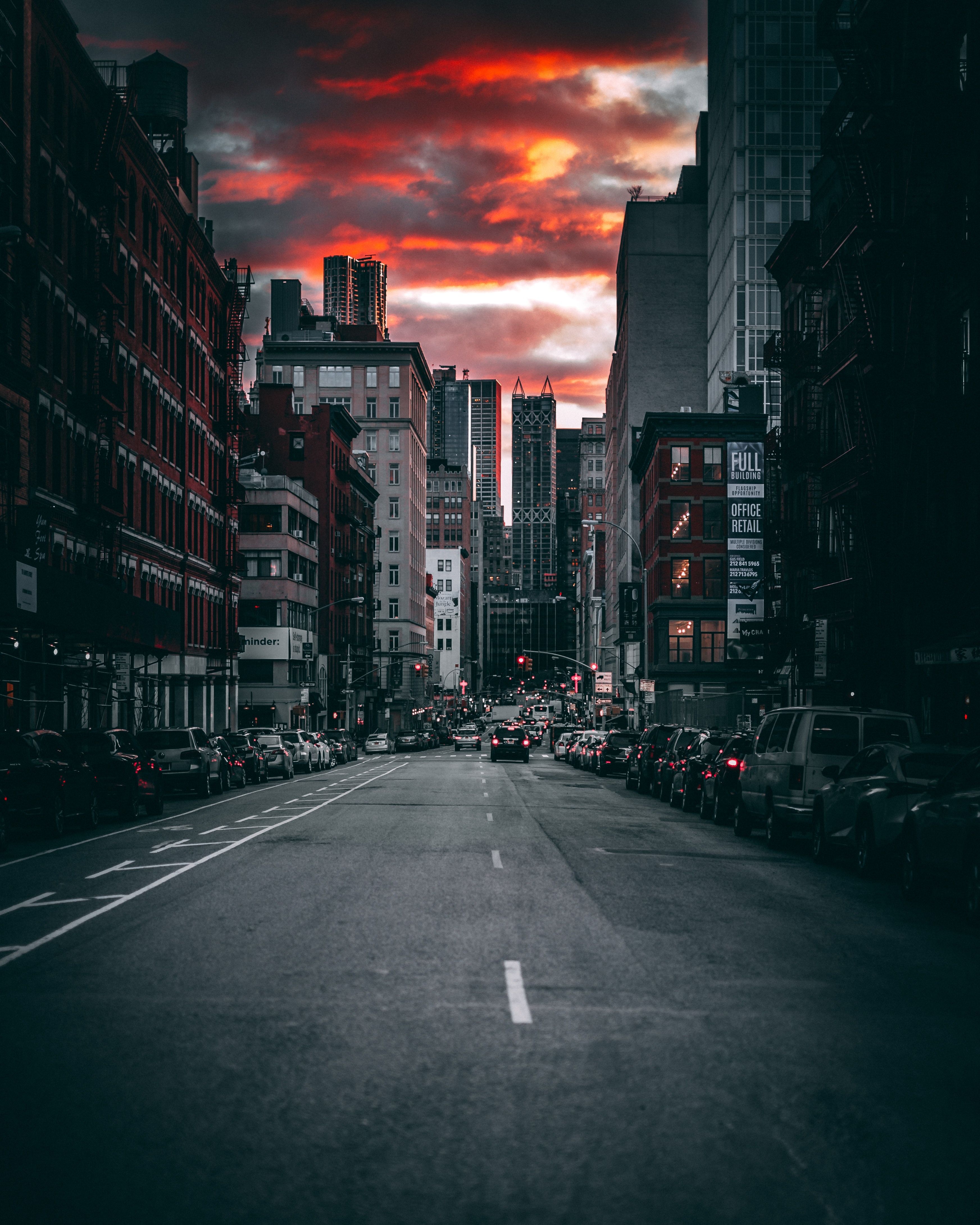 A city street at sunset with cars parked on the side of the road. - Cityscape