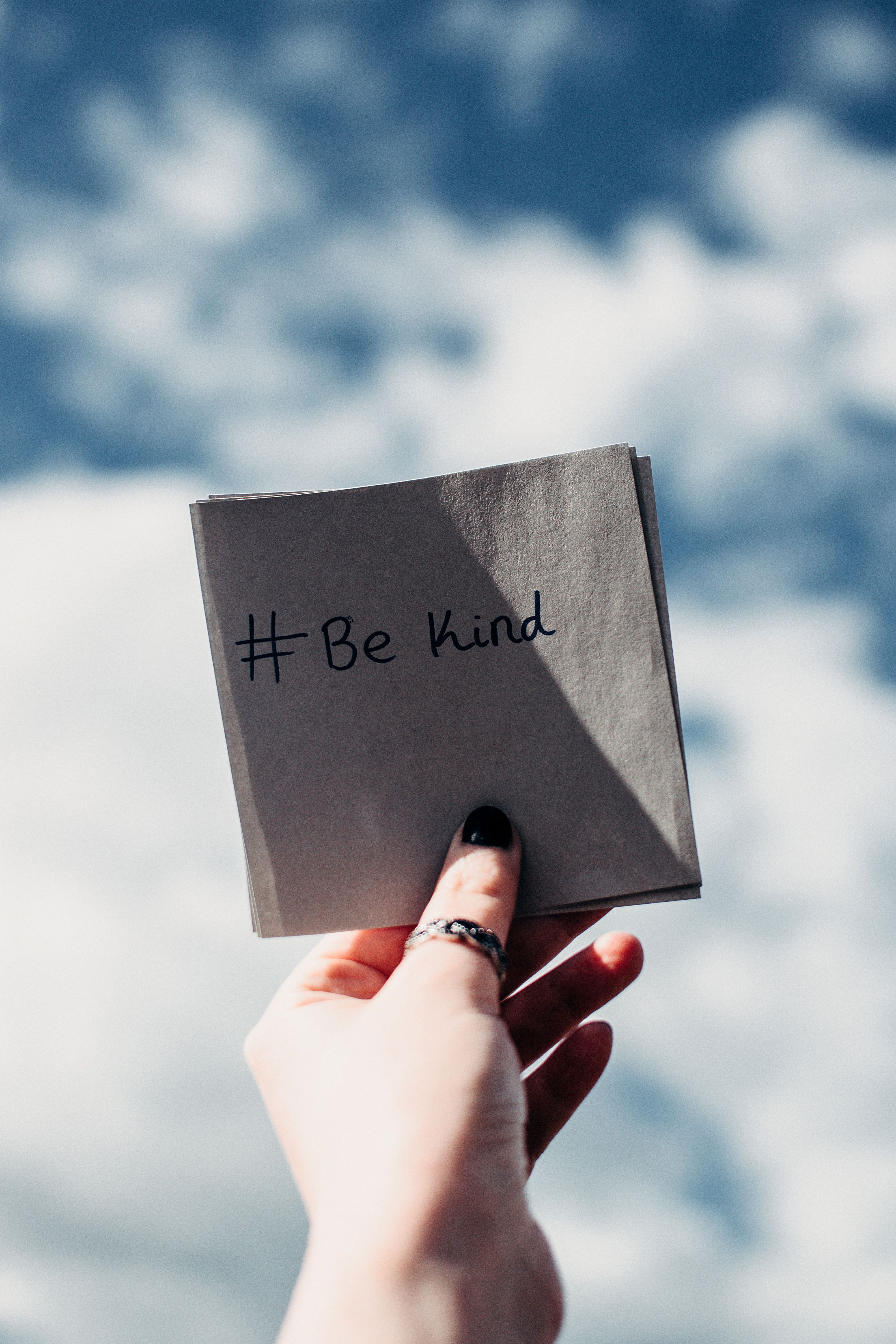 A hand holding a piece of paper with the hashtag Be Kind - Mental health