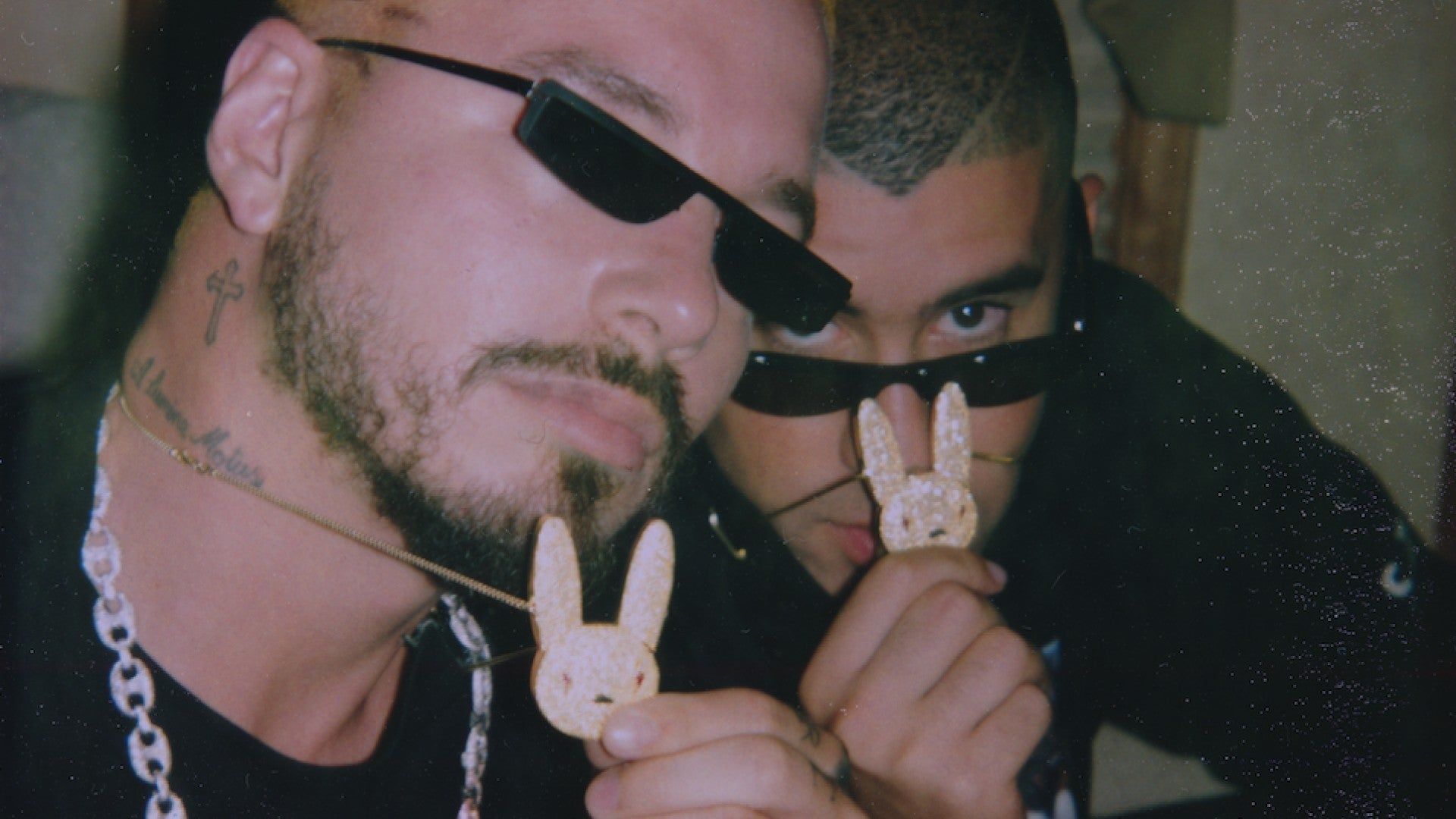 Two men wearing sunglasses holding up a white rabbit charm - Bad Bunny